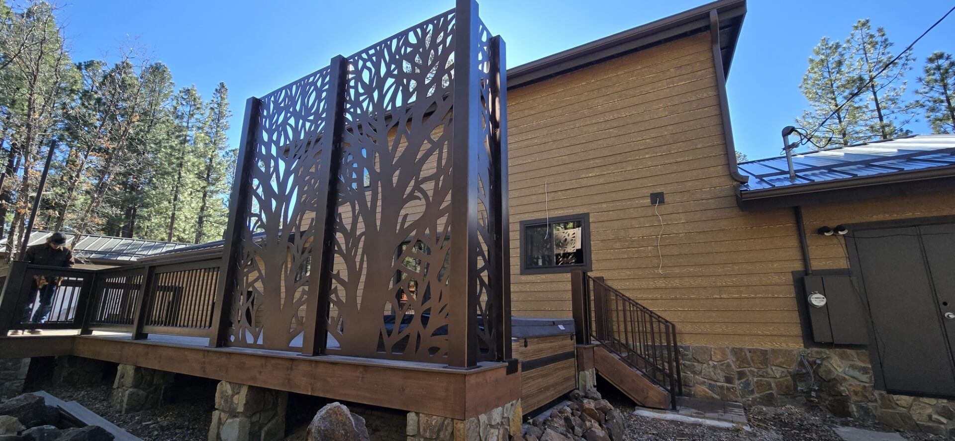 Wooden deck with decorative privacy panels beside a brick house under a clear blue sky