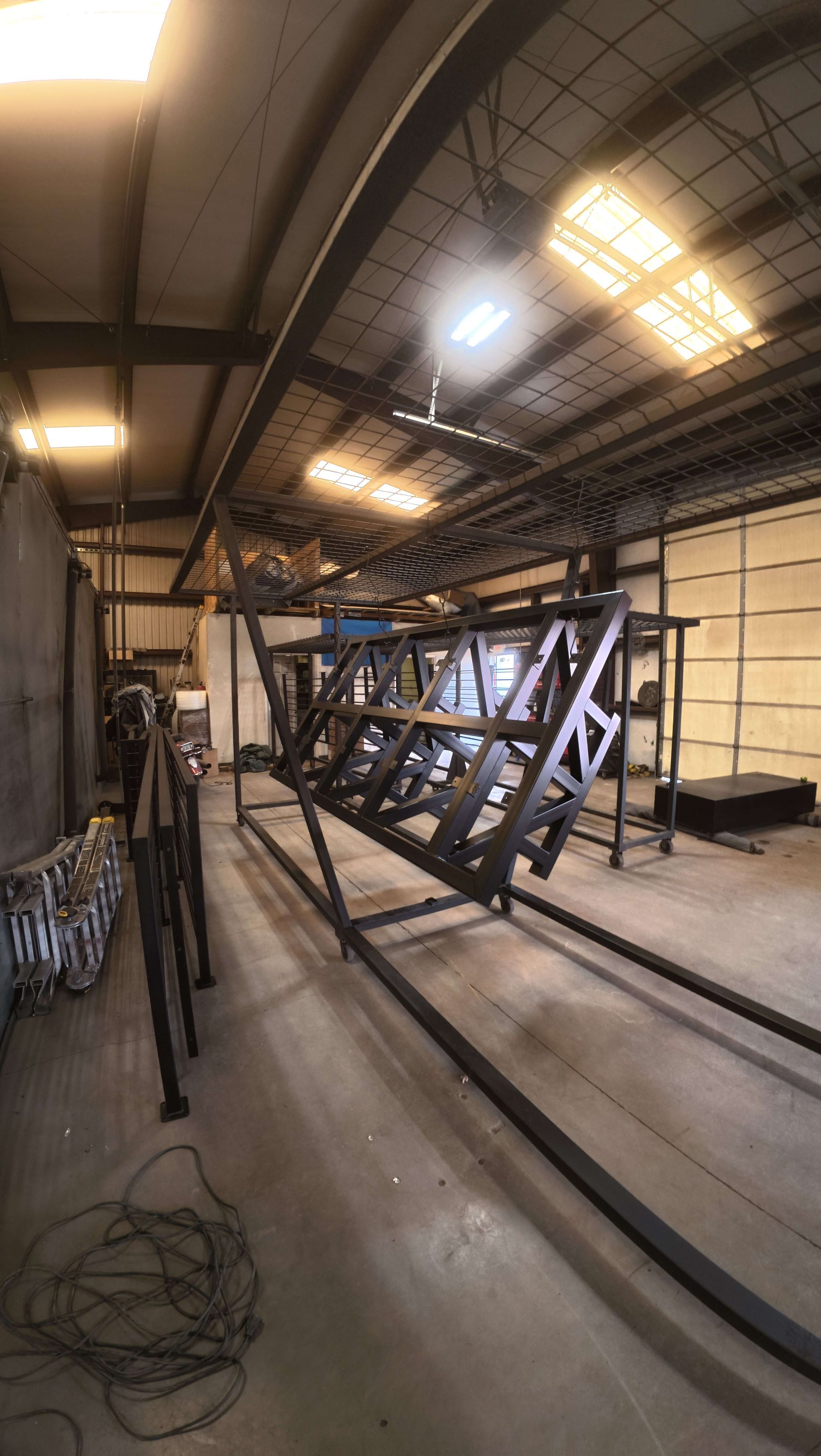Industrial workshop with a large metal truss frame on rails under bright overhead lights