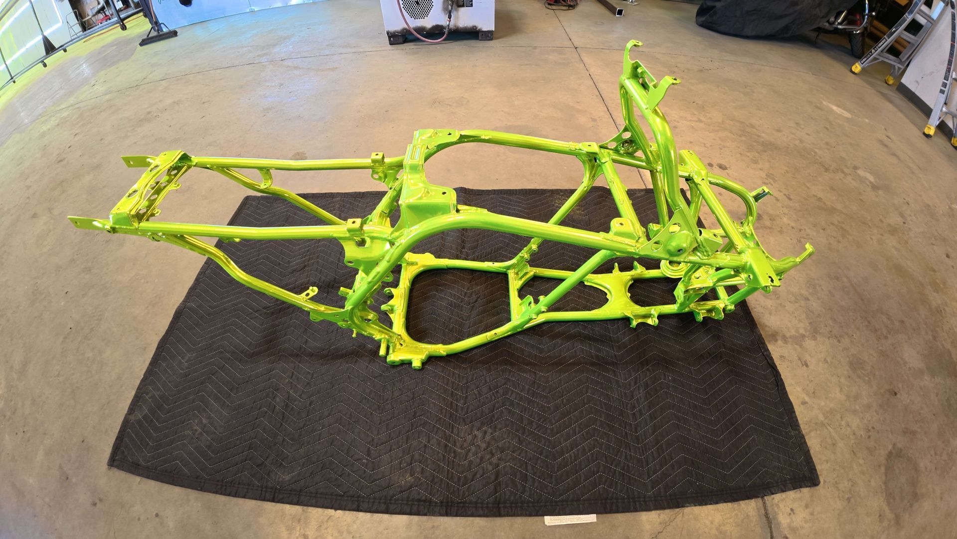 Bright green metal car frame chassis on a black mat in a workshop.