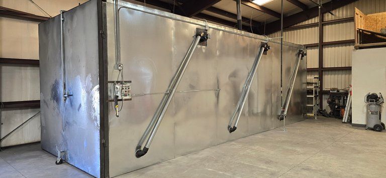 Industrial metal storage tank in a warehouse, with angled support arms and a gray concrete floor.