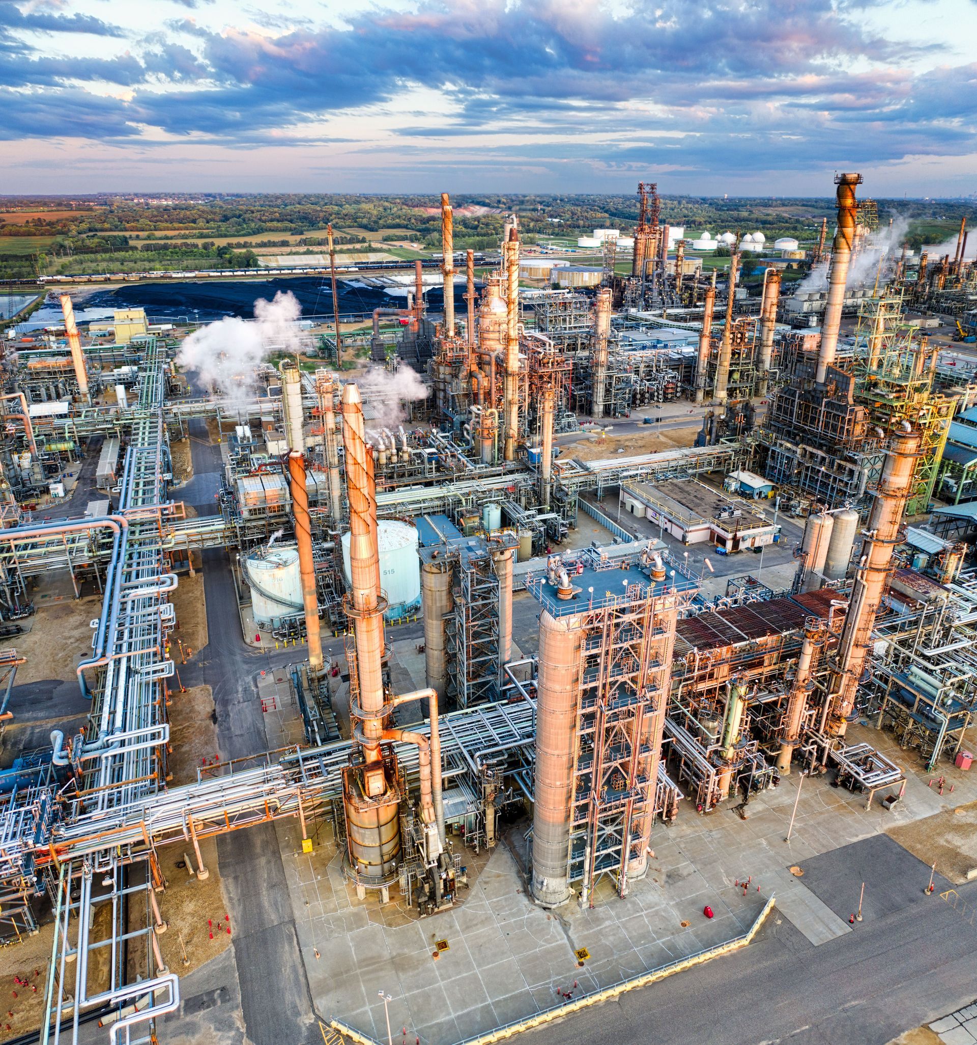 Aerial view of a sprawling industrial plant with pipes, towers, and steam under a cloudy sky