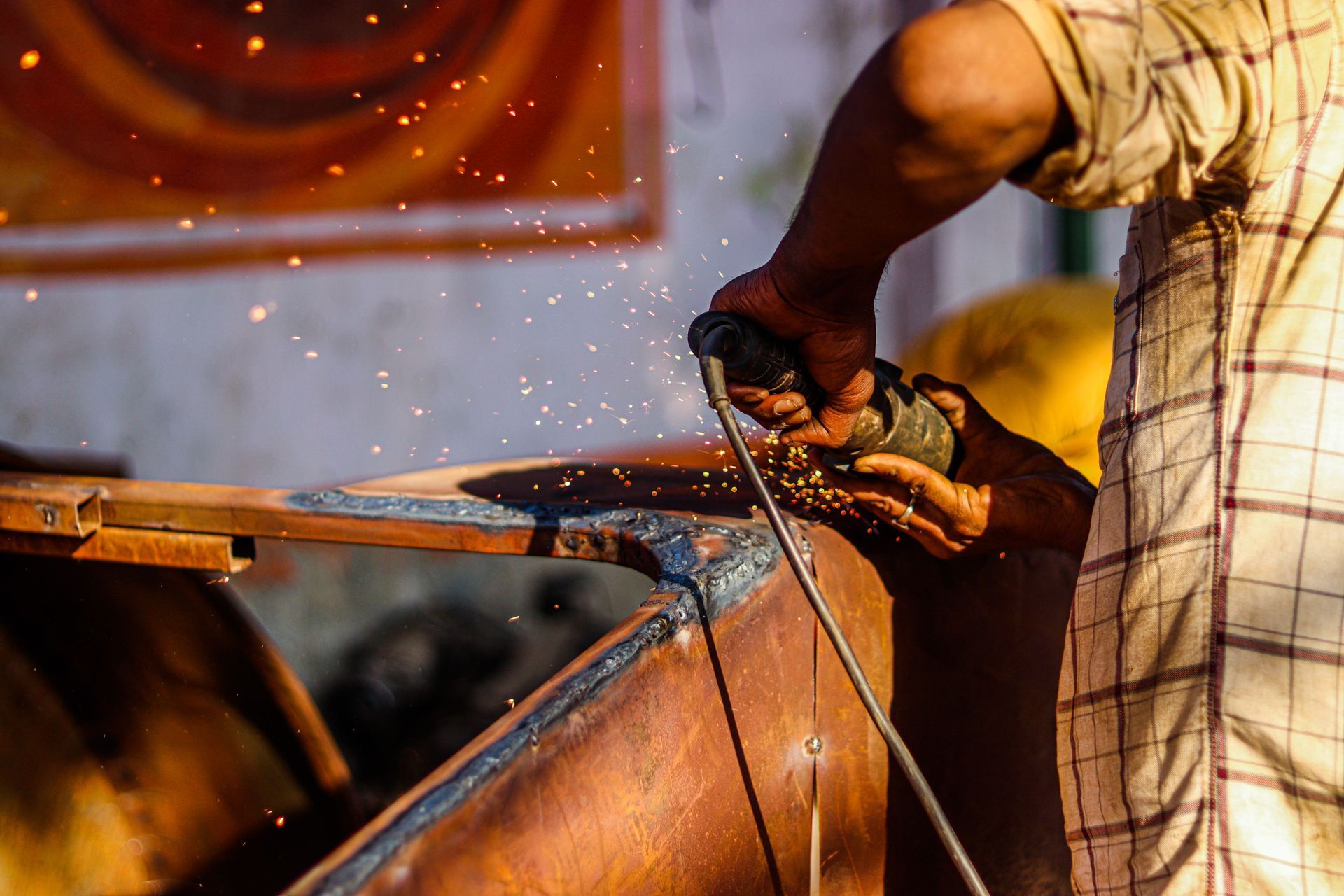 Close-up of a worker using a hand tool on metal, with sparks flying in a workshop