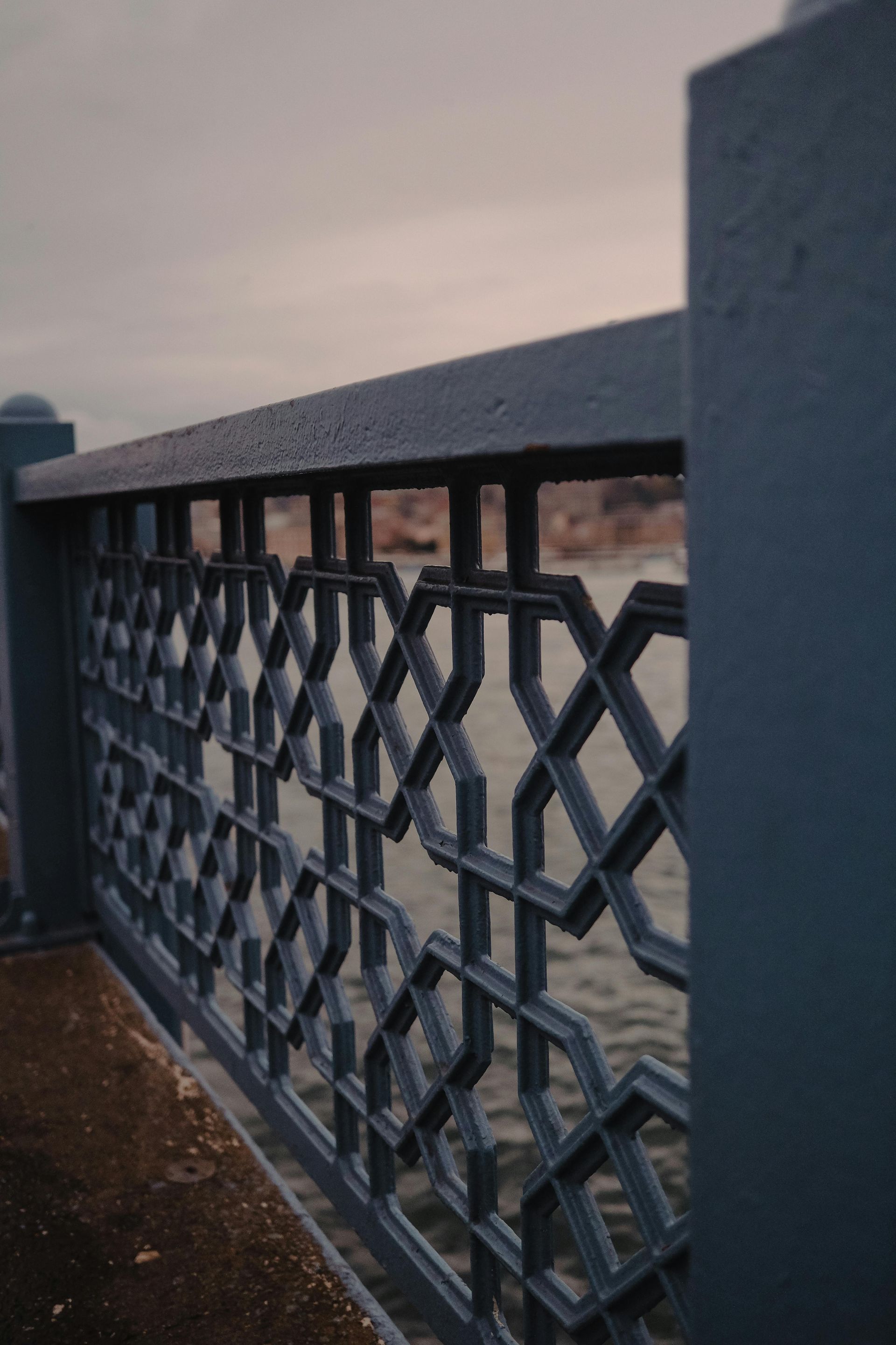 Decorative blue lattice railing with a dark top rail overlooking water at dusk