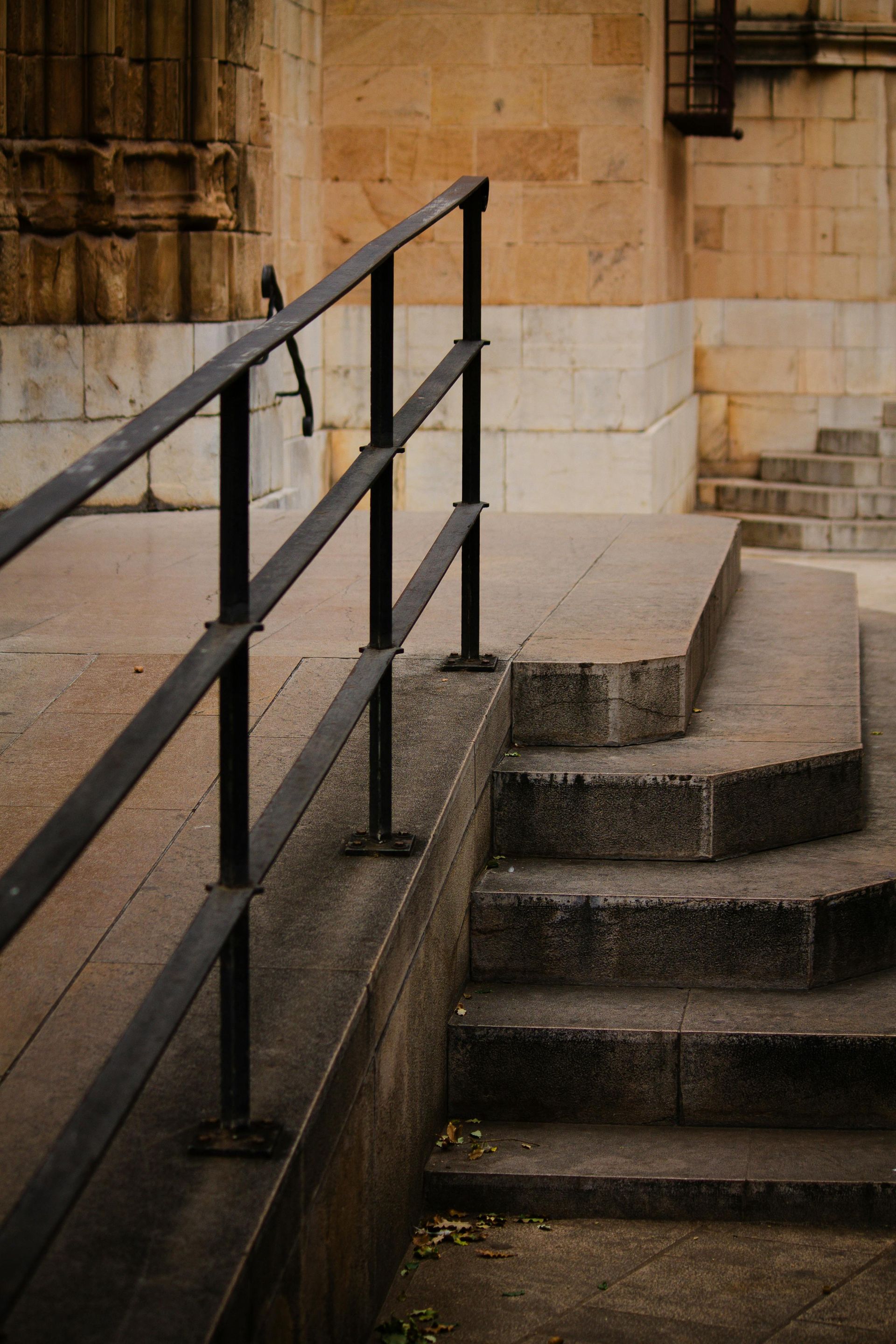 Staircase with black metal railings beside a tan stone wall and curved concrete steps
