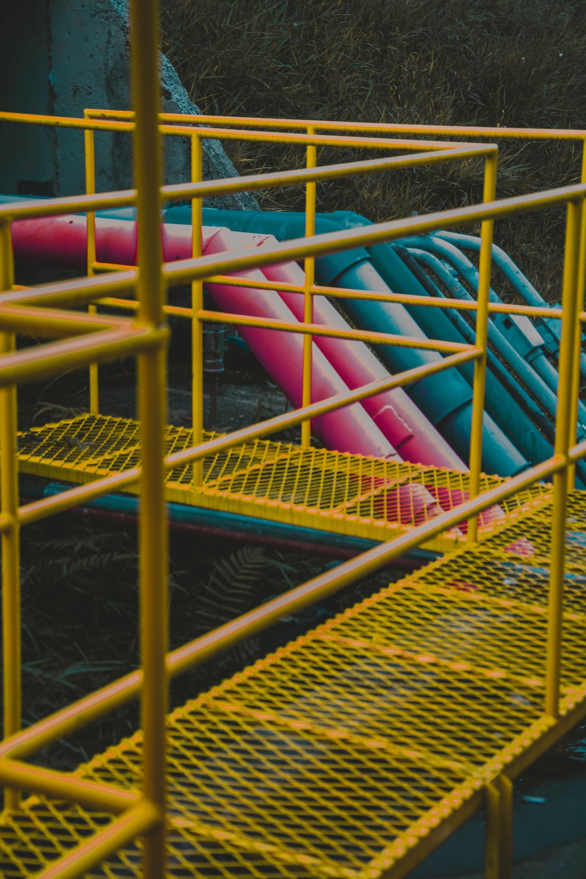 Yellow metal walkway with pink and blue pipes in an industrial setting
