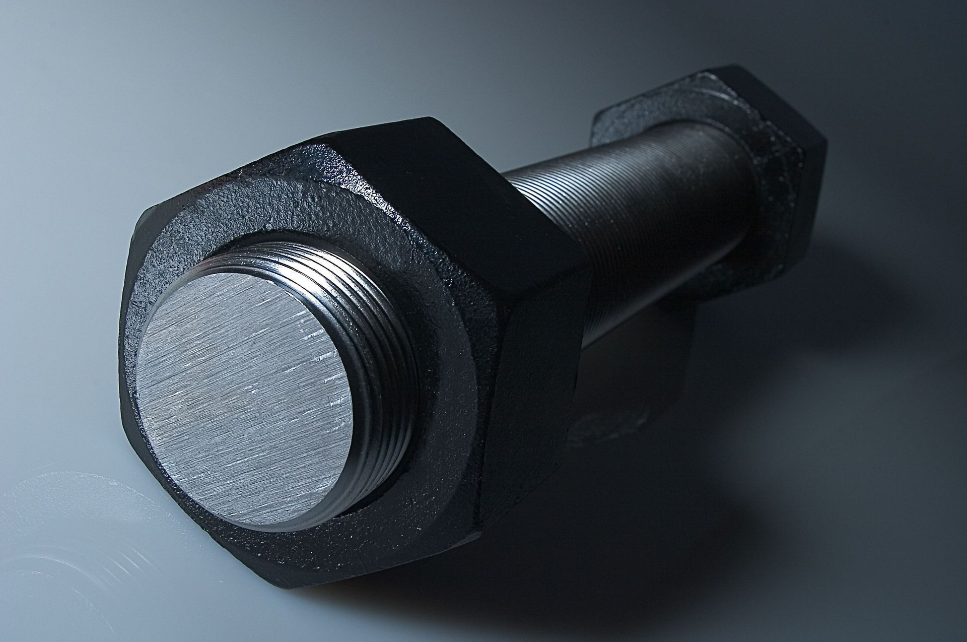 Black metal bolt with hex nut and threaded shaft on a gray surface