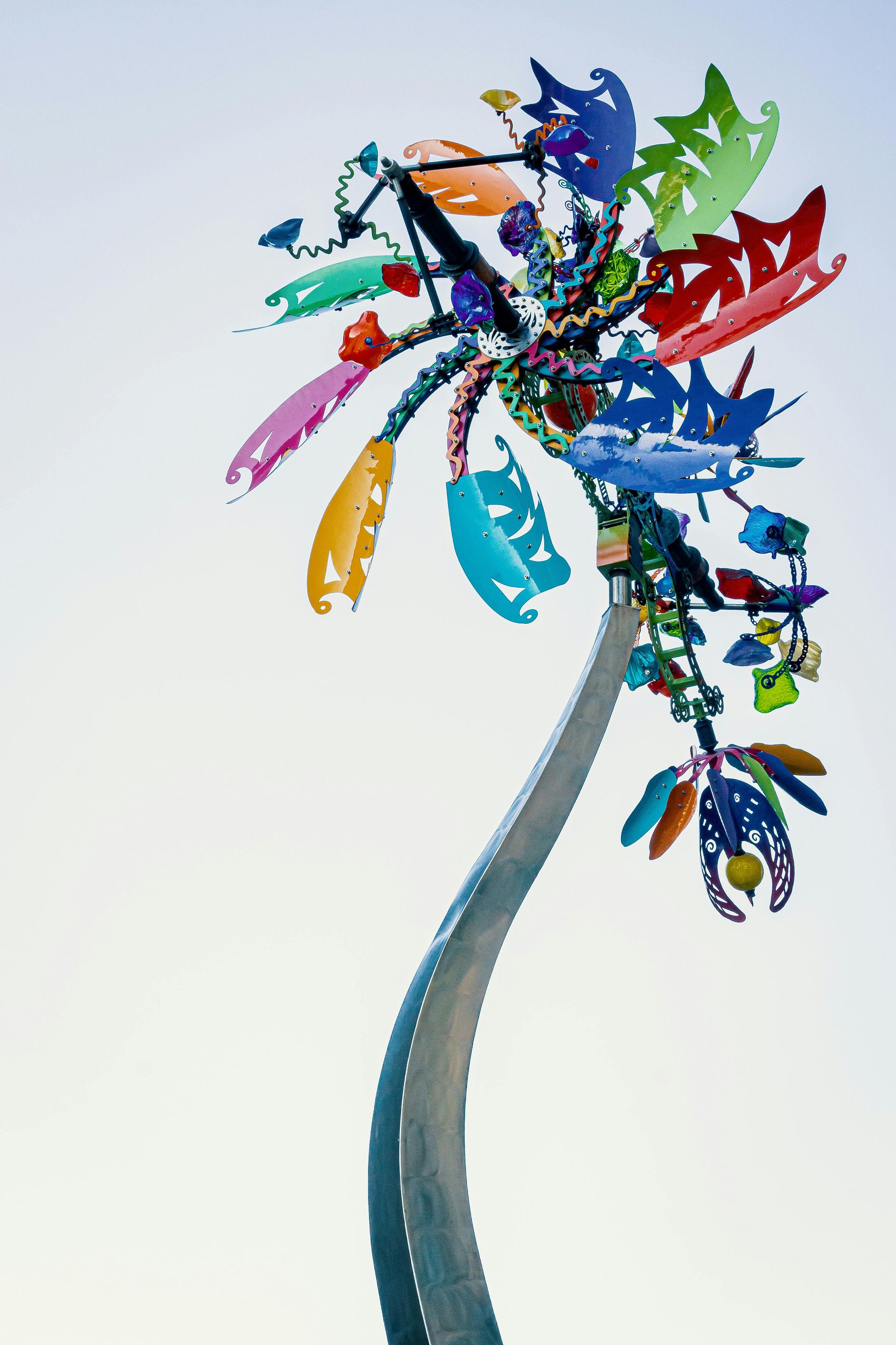 Abstract colorful bird sculpture with blue curved stem and multicolored feather-like shapes on a white background