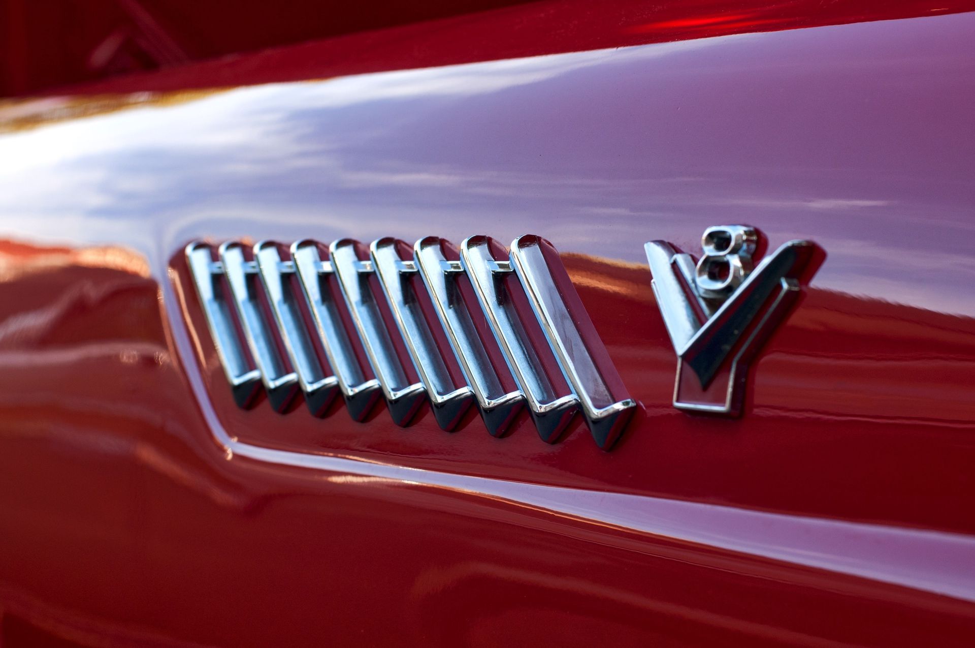 Close-up of a chrome V emblem and silver slashes on a red car hood