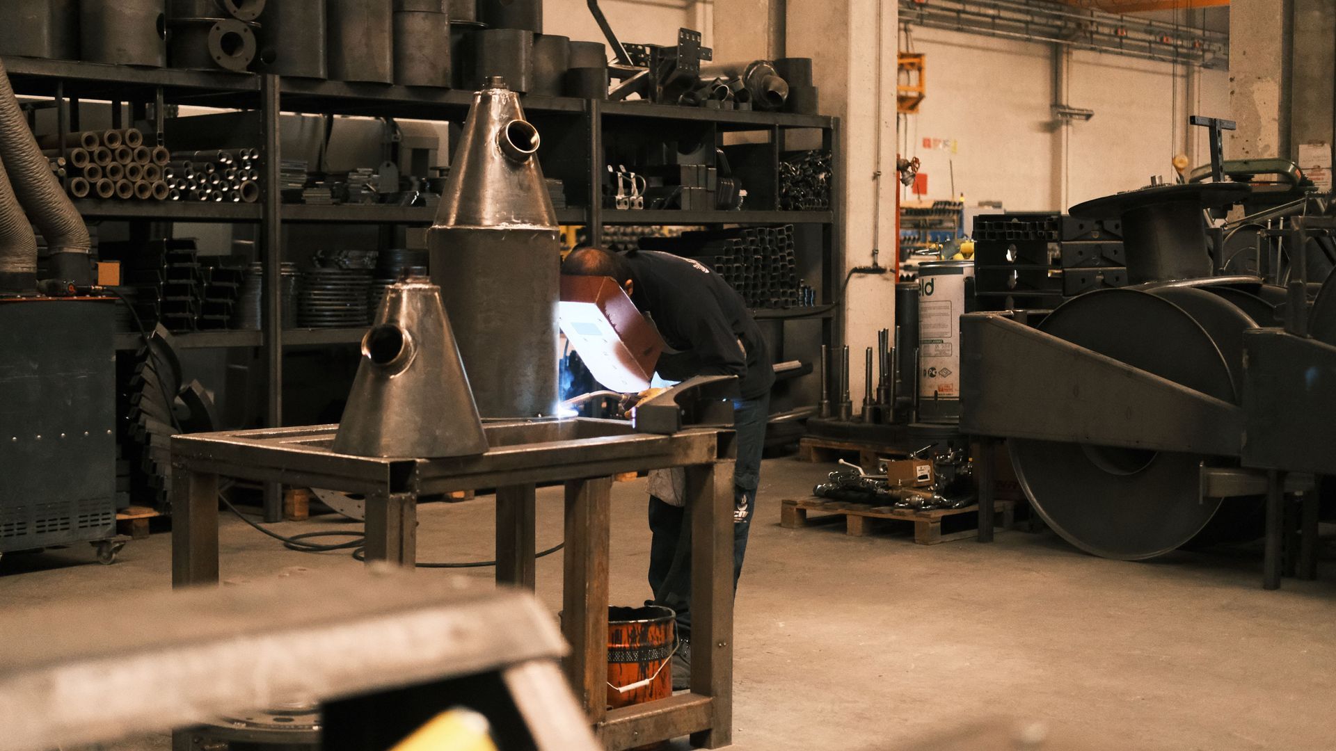 Person welding in an industrial workshop with large machinery and metal equipment.