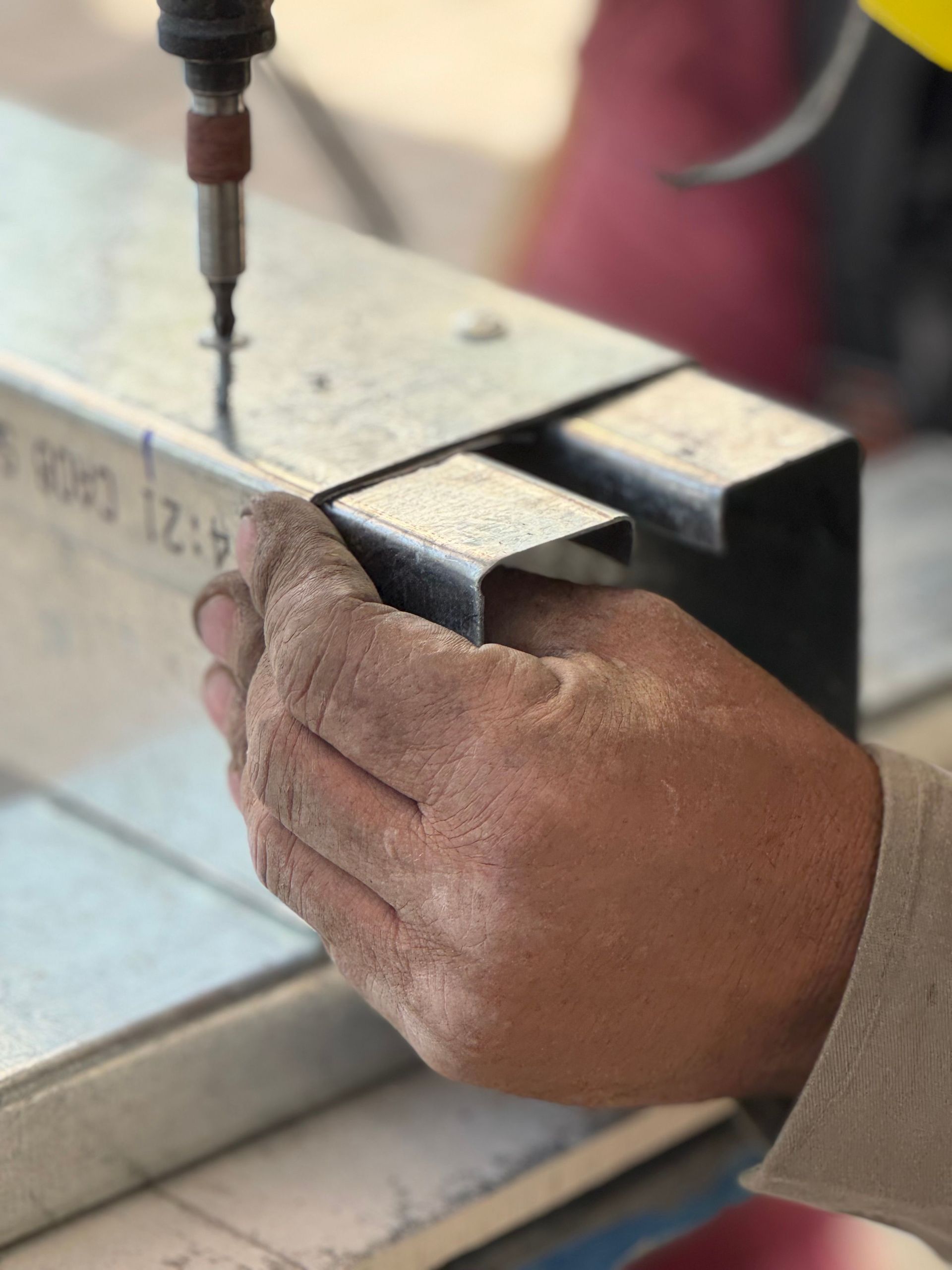 Worker holding a metal beam while drilling a hole in a workshop