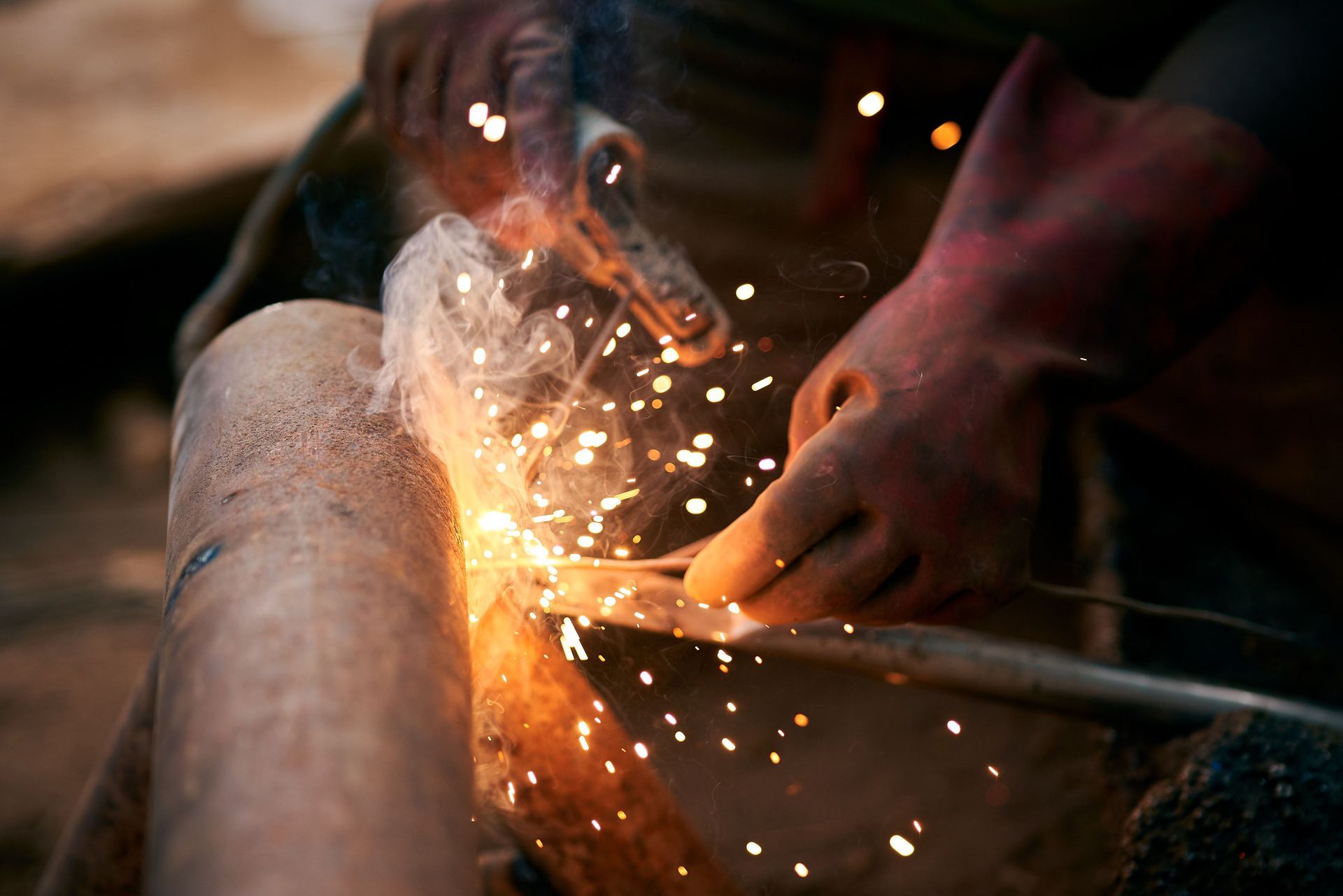 Person welding metal, sending bright sparks in a dim workshop.