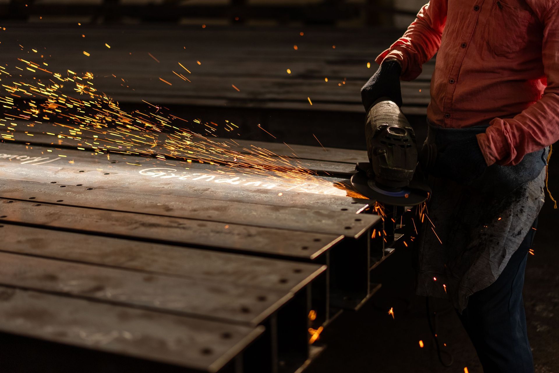 Worker using a grinder on a metal surface, sending bright sparks in a workshop