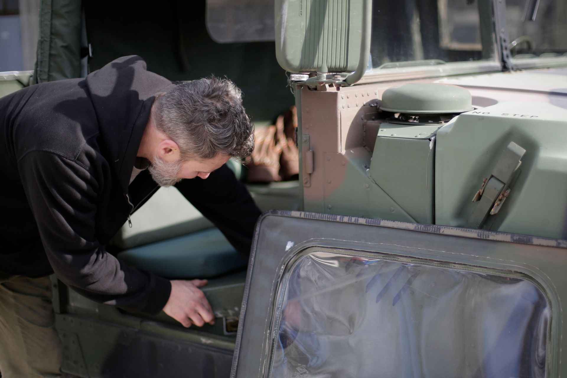 Person inspecting the interior of a green military vehicle outdoors