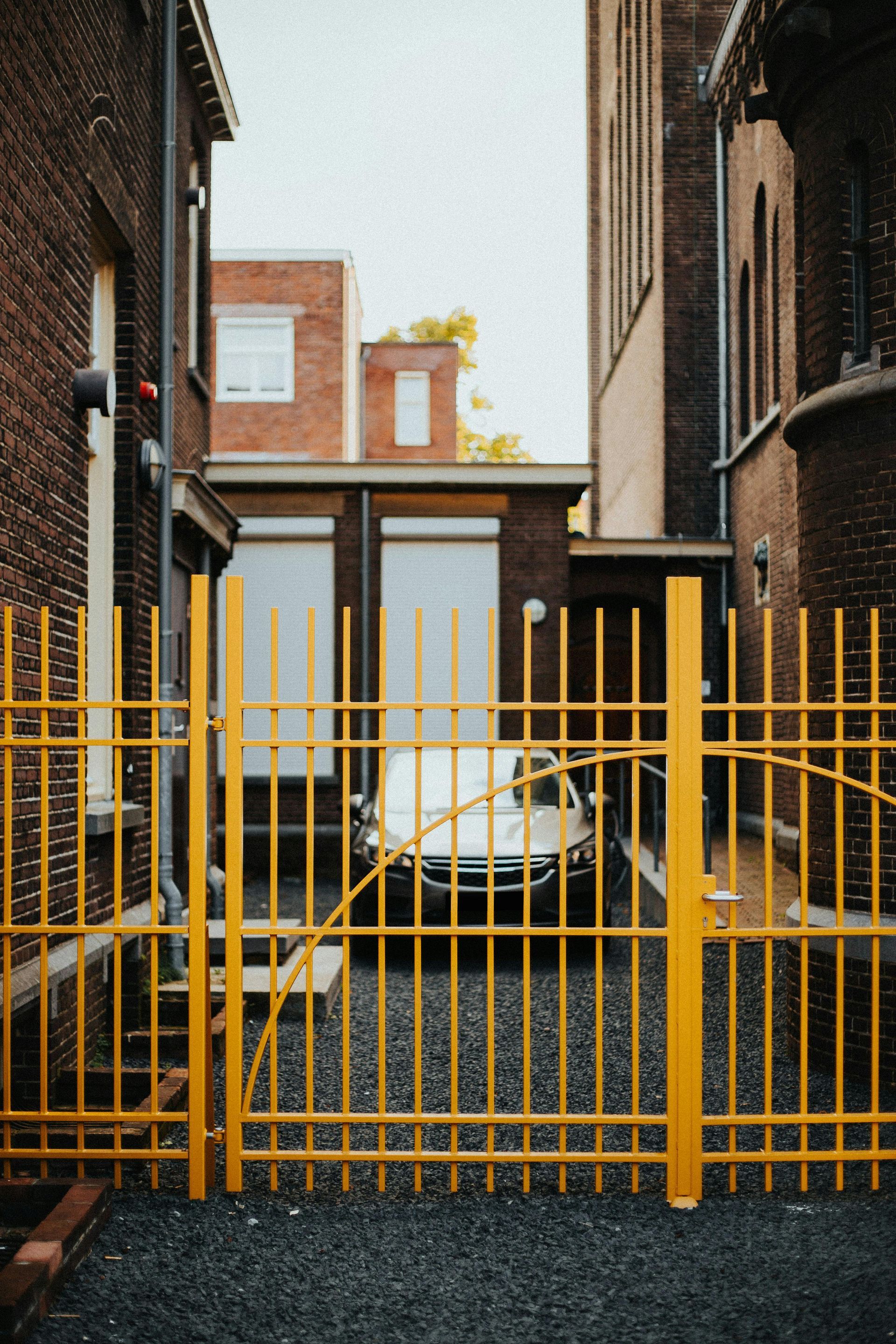 Yellow metal gate blocking a narrow alley with a white car parked behind it between brick buildings