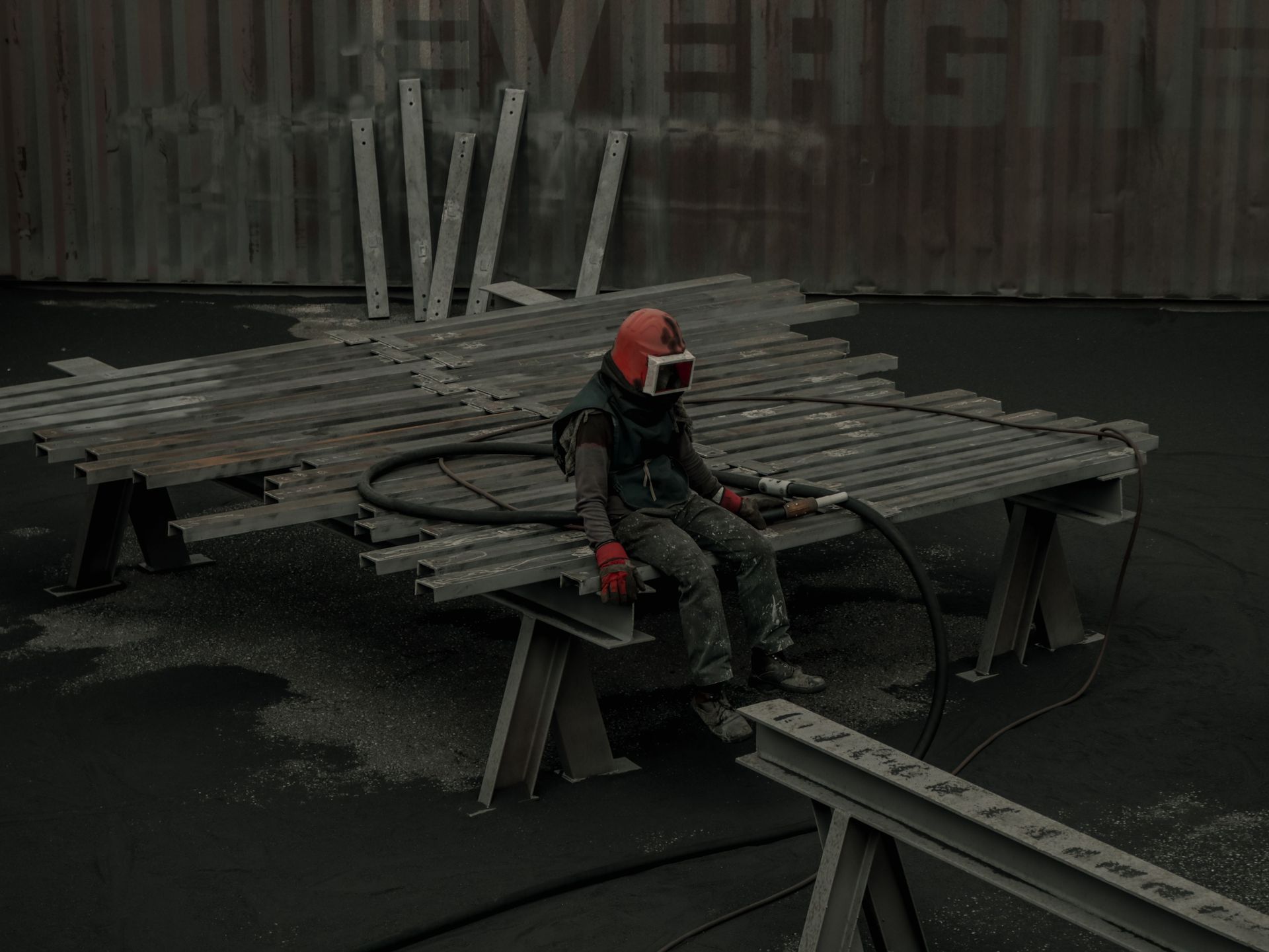 Worker in orange helmet sits on scaffolding at a construction site.