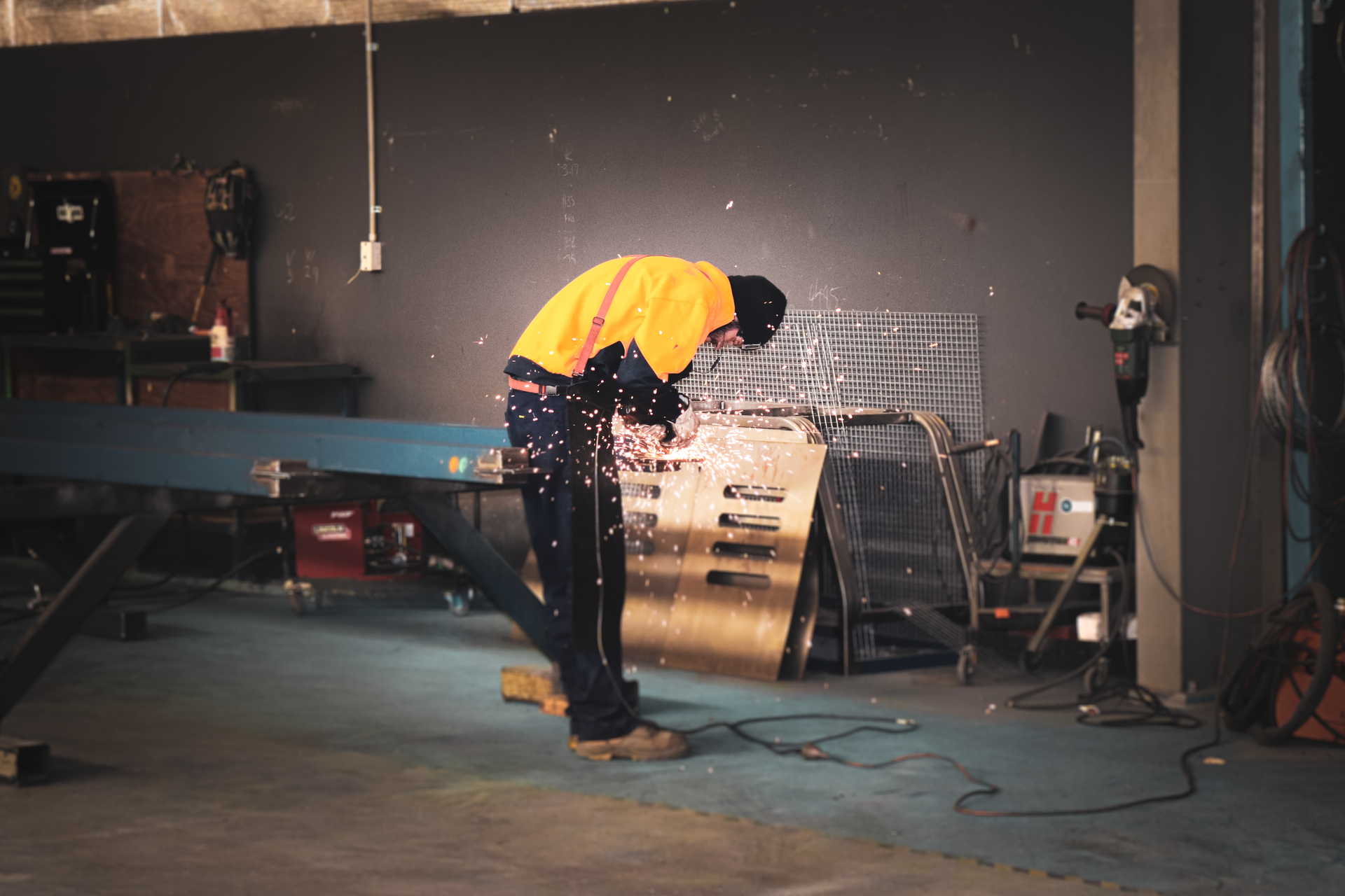 Person in a yellow jacket bending over a drum set in a dim rehearsal studio