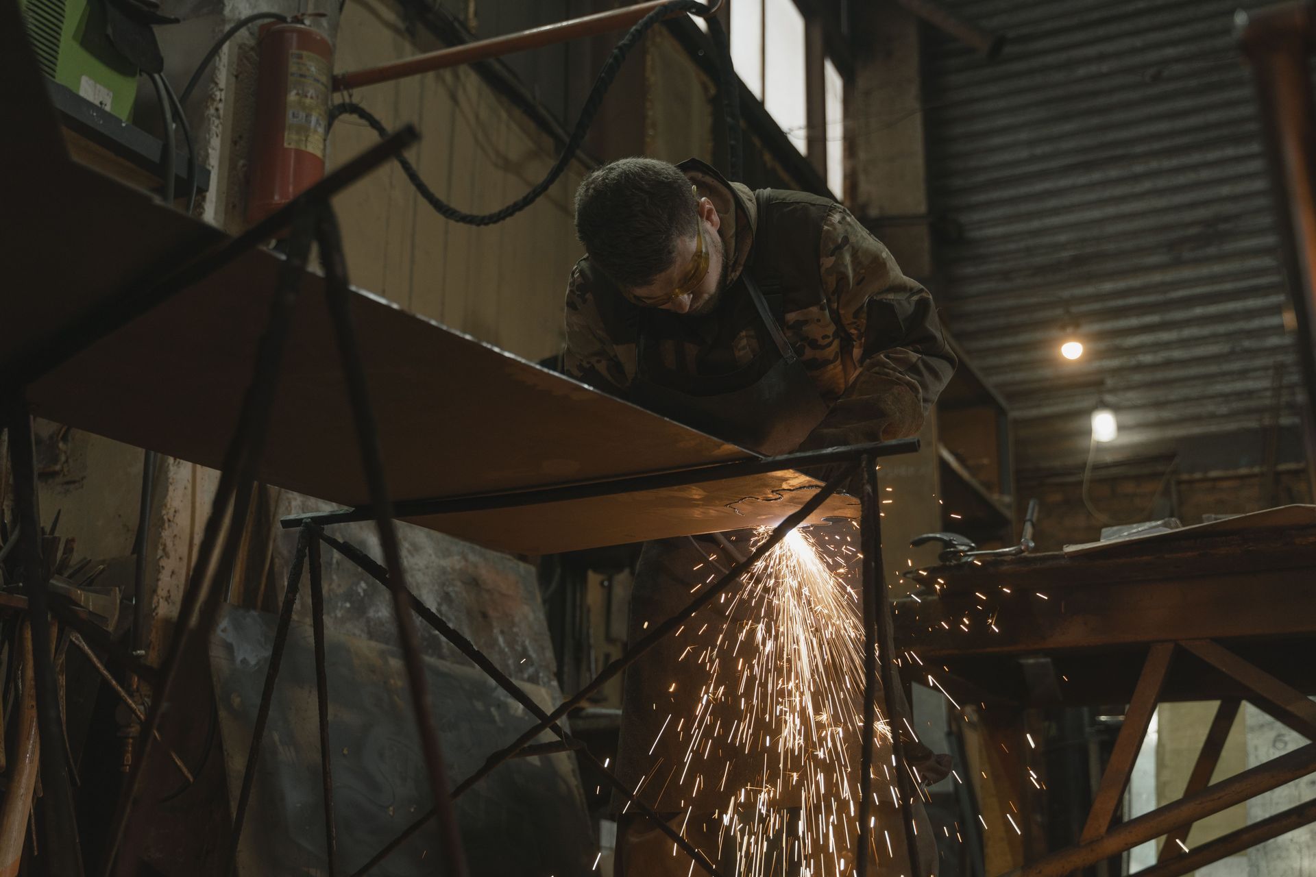 Worker welding metal on a scaffold indoors, with bright sparks flying in a dim workshop.