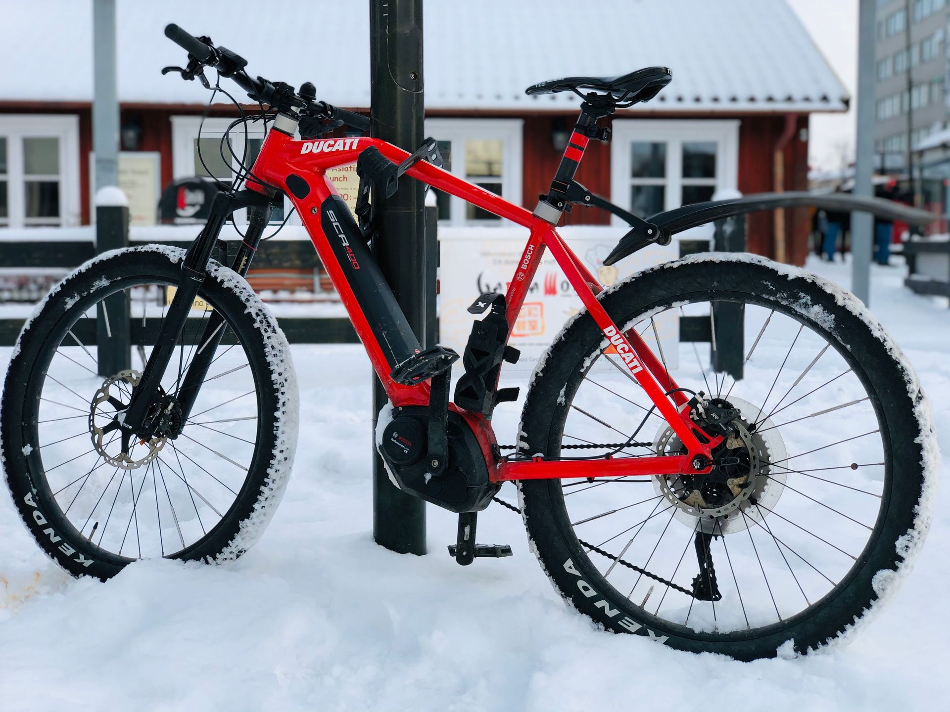 Red electric mountain bike parked against a pole outdoors in the snow