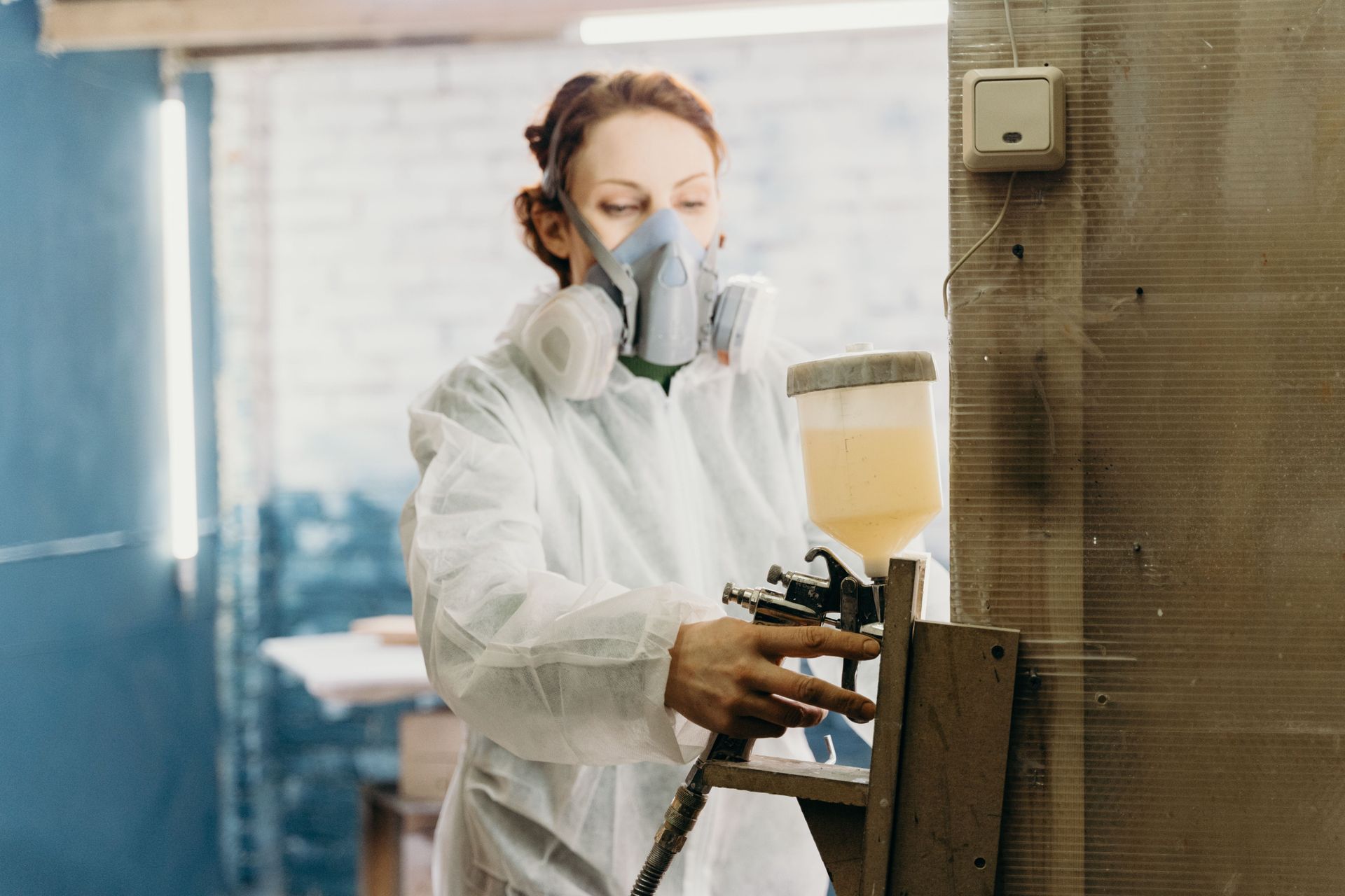 Worker in protective suit and respirator spray-painting a metal surface in a workshop