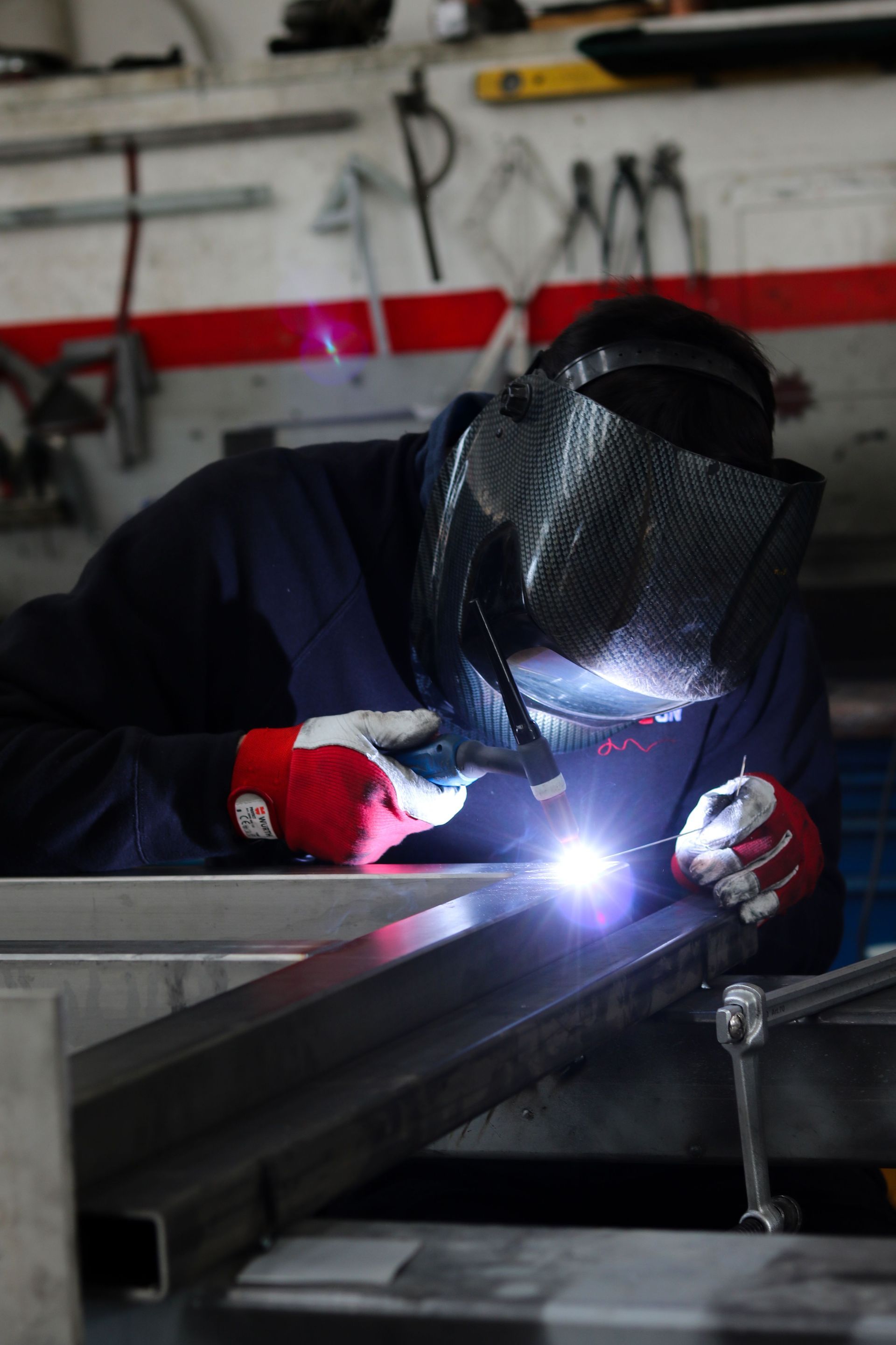 Welder in mask and gloves welding a metal beam, bright arc light in workshop