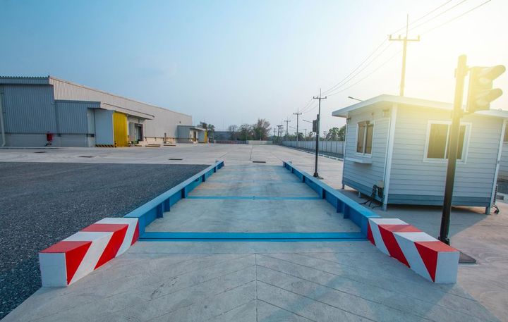 An industrial truck scale with blue sides and red-and-white striped barriers, located next to a small security guard booth.