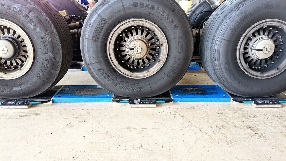 Three large aircraft tires resting on blue weighing scales on a concrete floor.