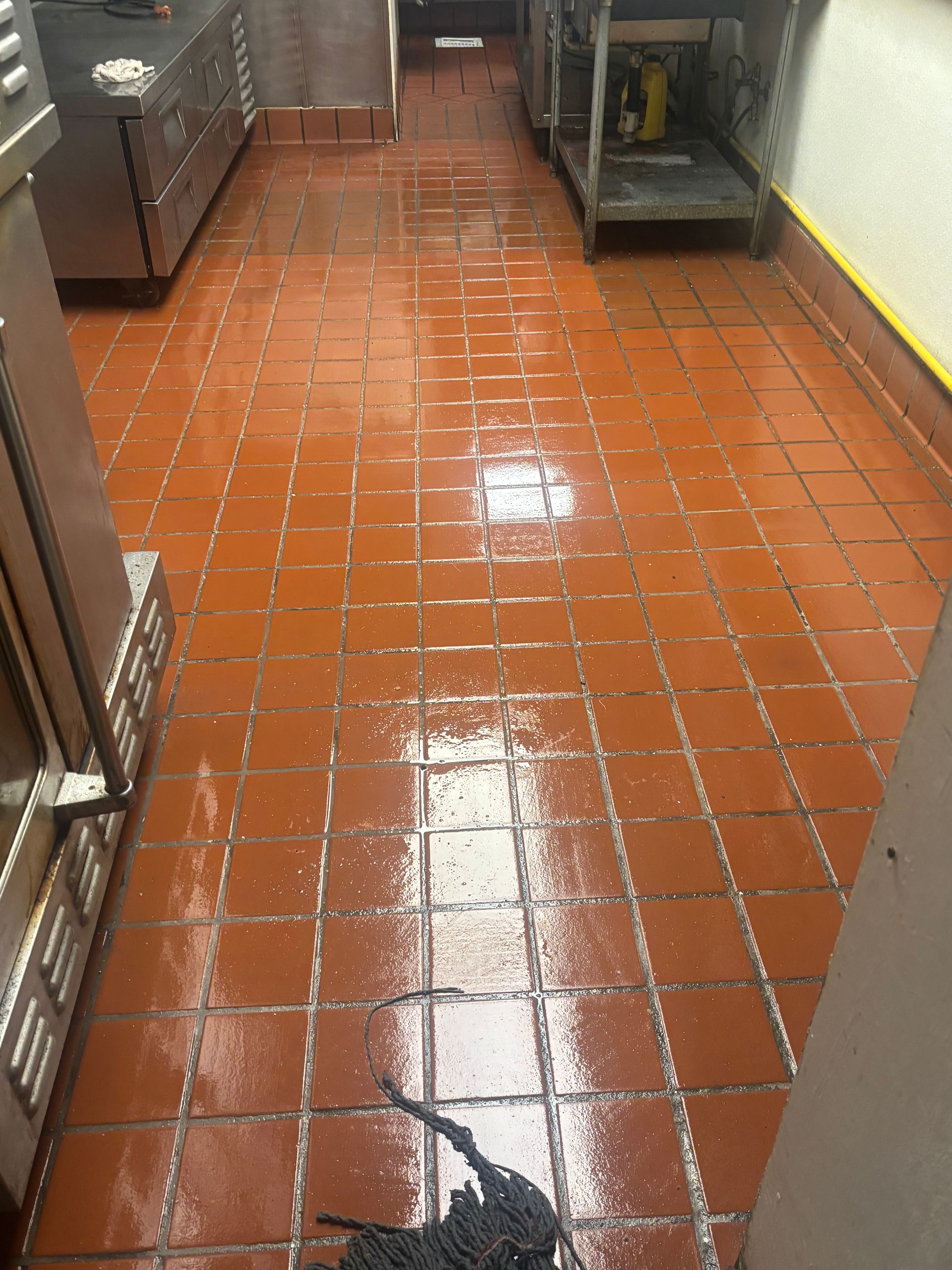 Hands wearing orange rubber gloves use a yellow sponge to clean a black glass stovetop.