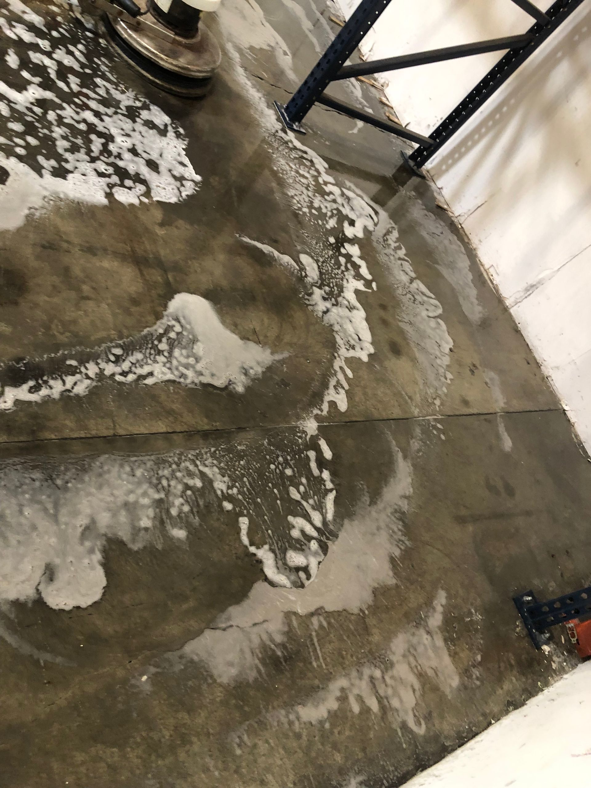 A worker in blue overalls uses a carpet cleaning machine to vacuum a light-colored rug in a bright, modern room.