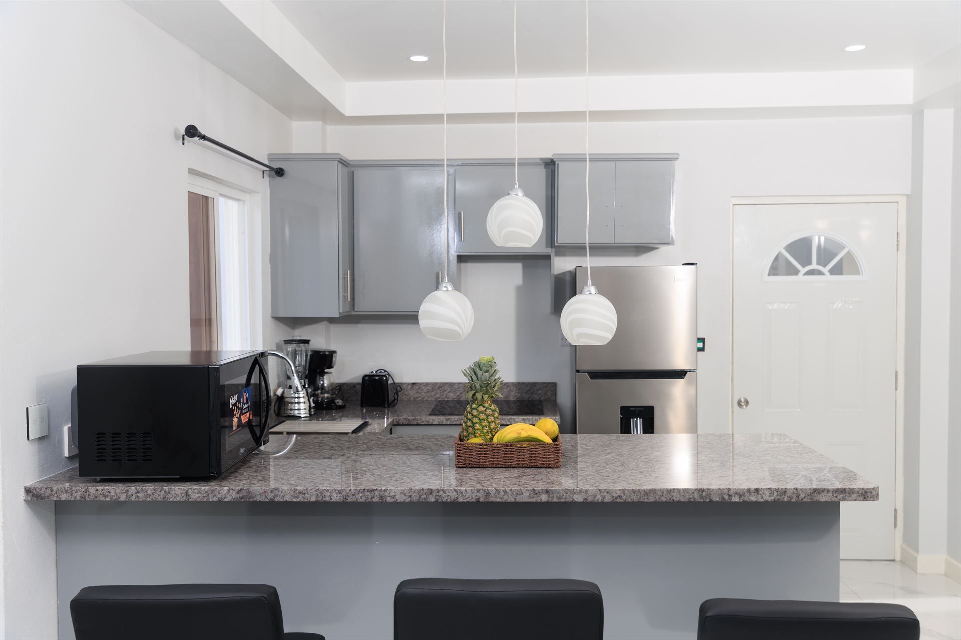 A kitchen with a stainless steel refrigerator , microwave , sink , and bar stools.