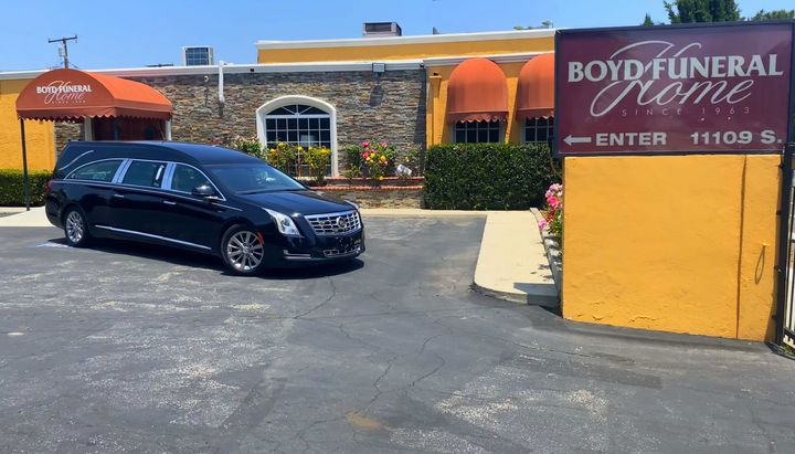Black minivan parked outside Boyd Funeral Home in front of a yellow sign and brick building.