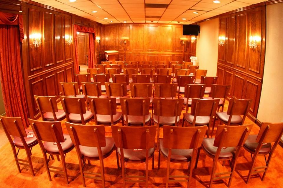 Empty wood-paneled conference room with rows of chairs facing a front table, warmly lit in orange tones