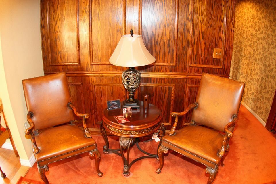 Two brown leather chairs flank a round wooden table with lamp in a wood-paneled room.