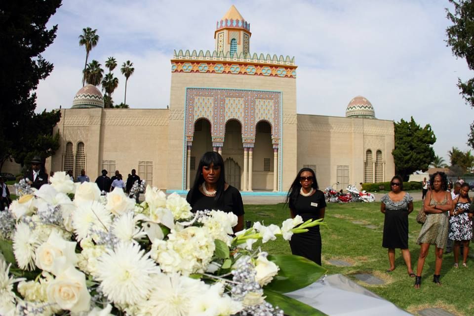People standing on a lawn before a decorative building, with large white flowers in the foreground.