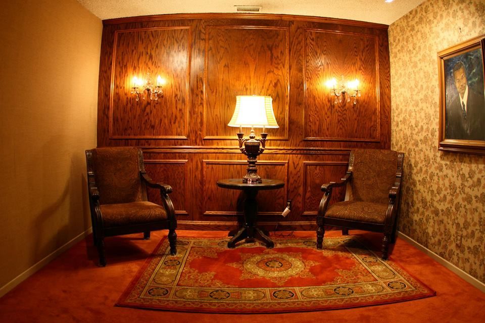 Cozy wood-paneled room with two armchairs, a table lamp, and patterned rug.