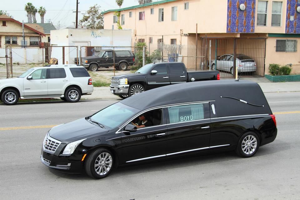 Black hearse driving on a street beside parked cars and apartment buildings