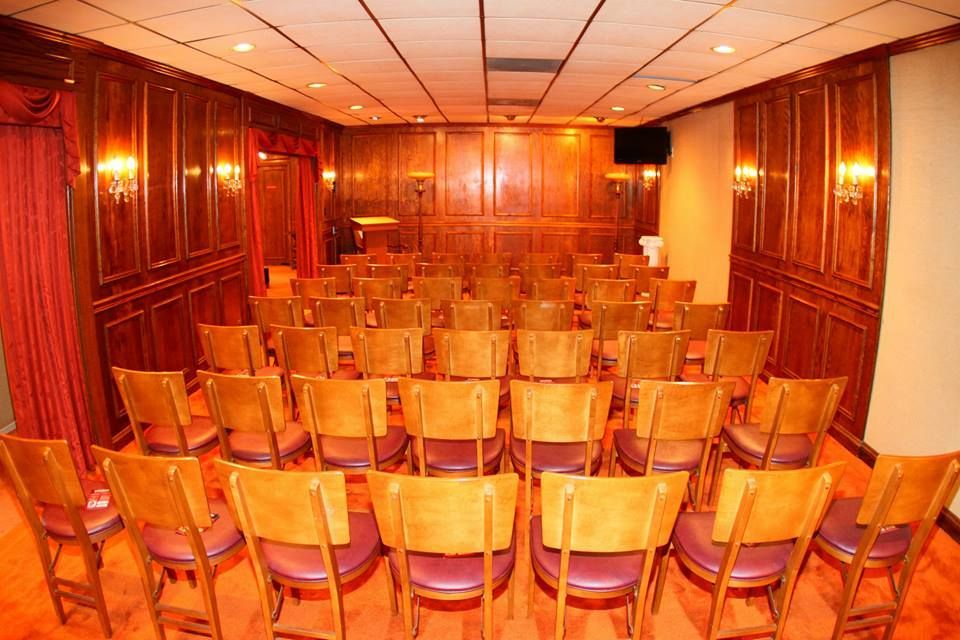 Empty conference room with rows of wooden chairs facing the front, lit by warm orange lights.