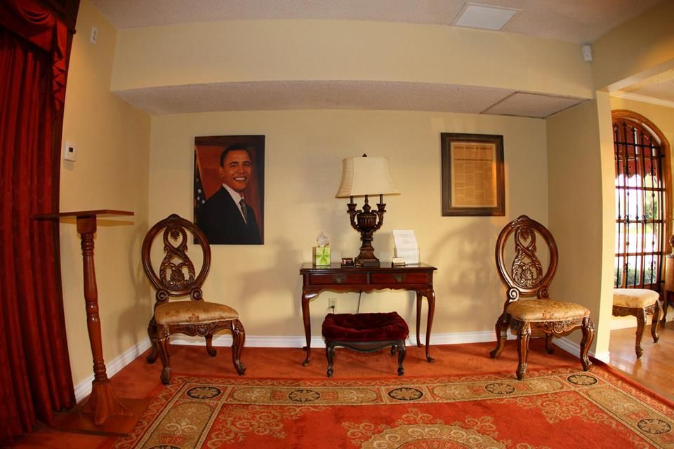 Formal room with ornate chairs, red rug, framed portrait, and a side table with lamp and candles