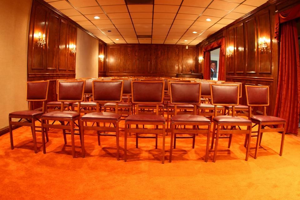 Empty wooden stage with chairs in front, warm orange lighting, and wood-paneled walls