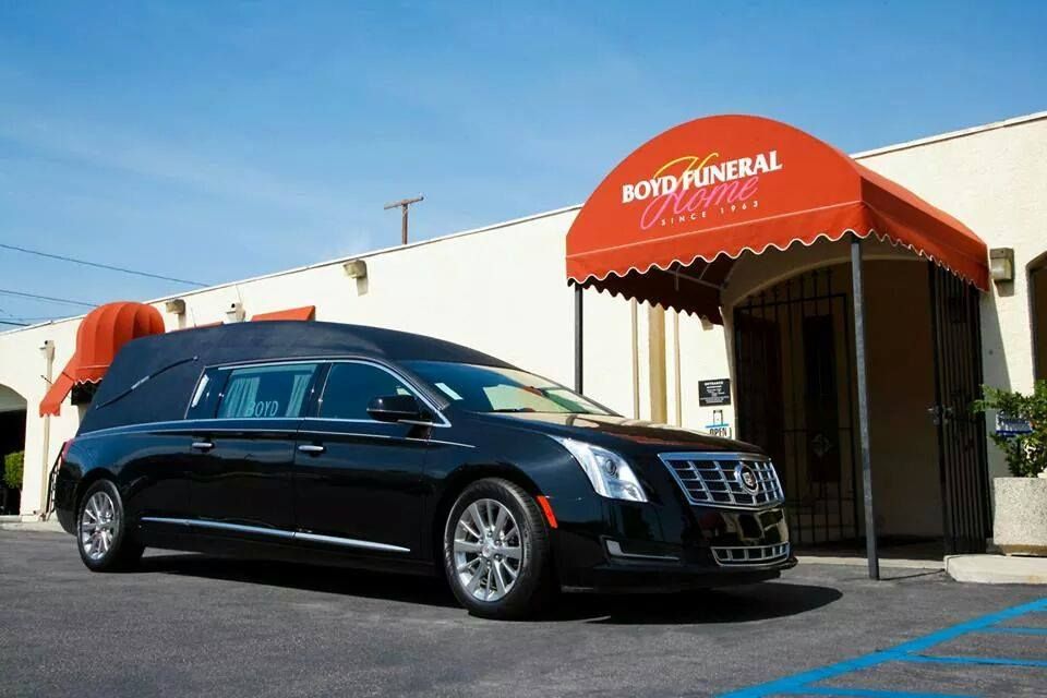 Black hearse parked outside a funeral home with a red awning under a clear blue sky