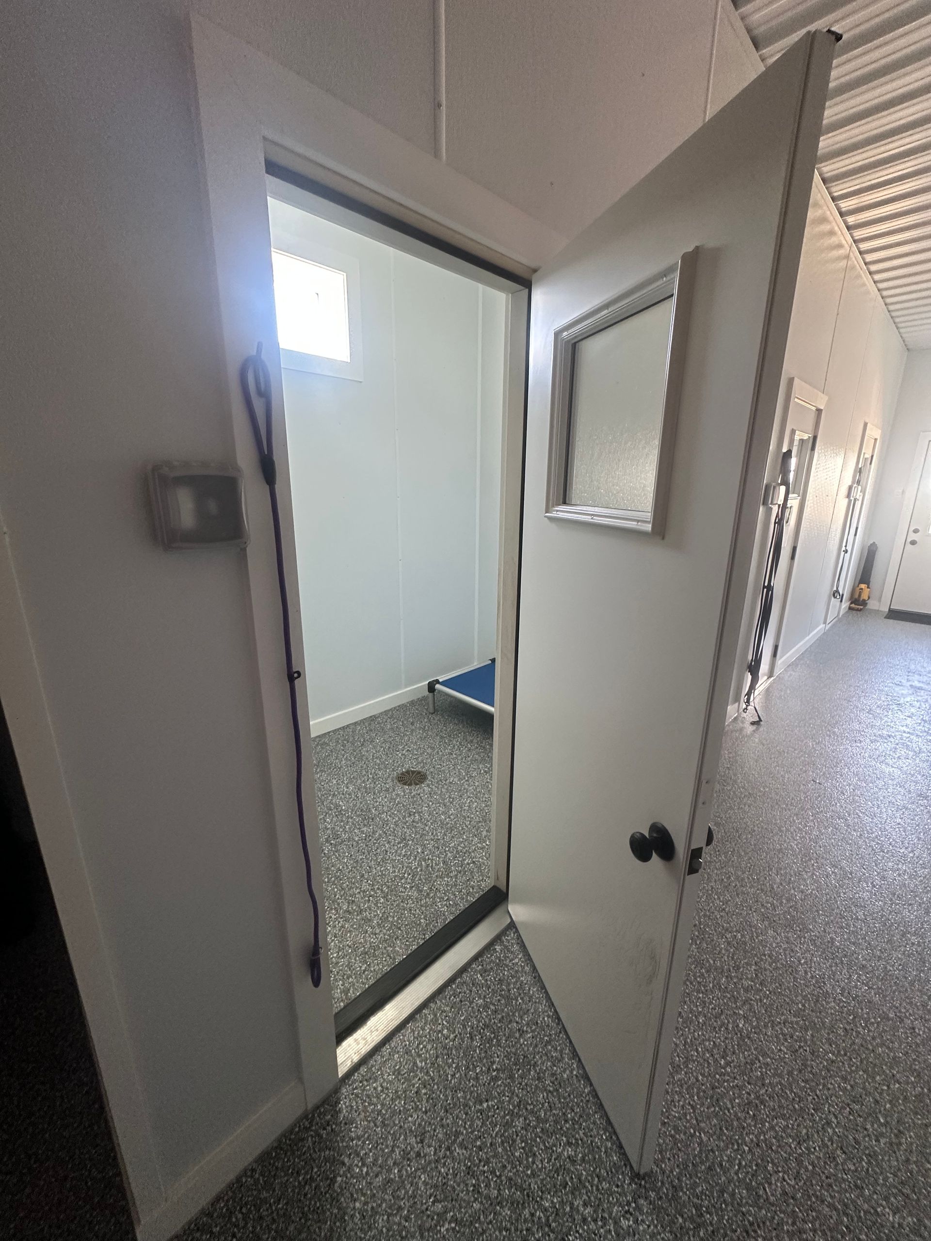 Open white door reveals a small, clean room with a pet bed. The floor is speckled gray.