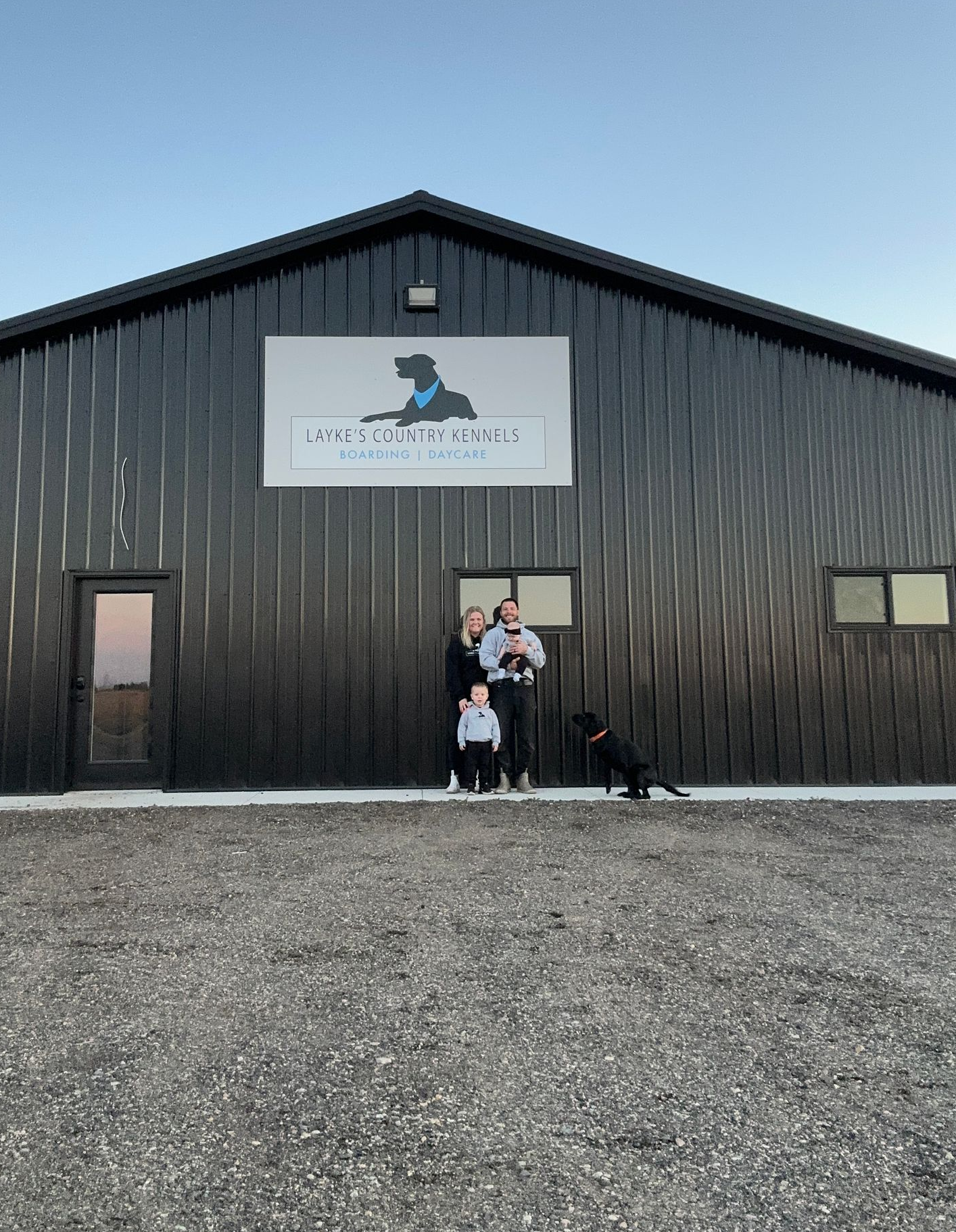 Family and black dog in front of black building with sign that says 