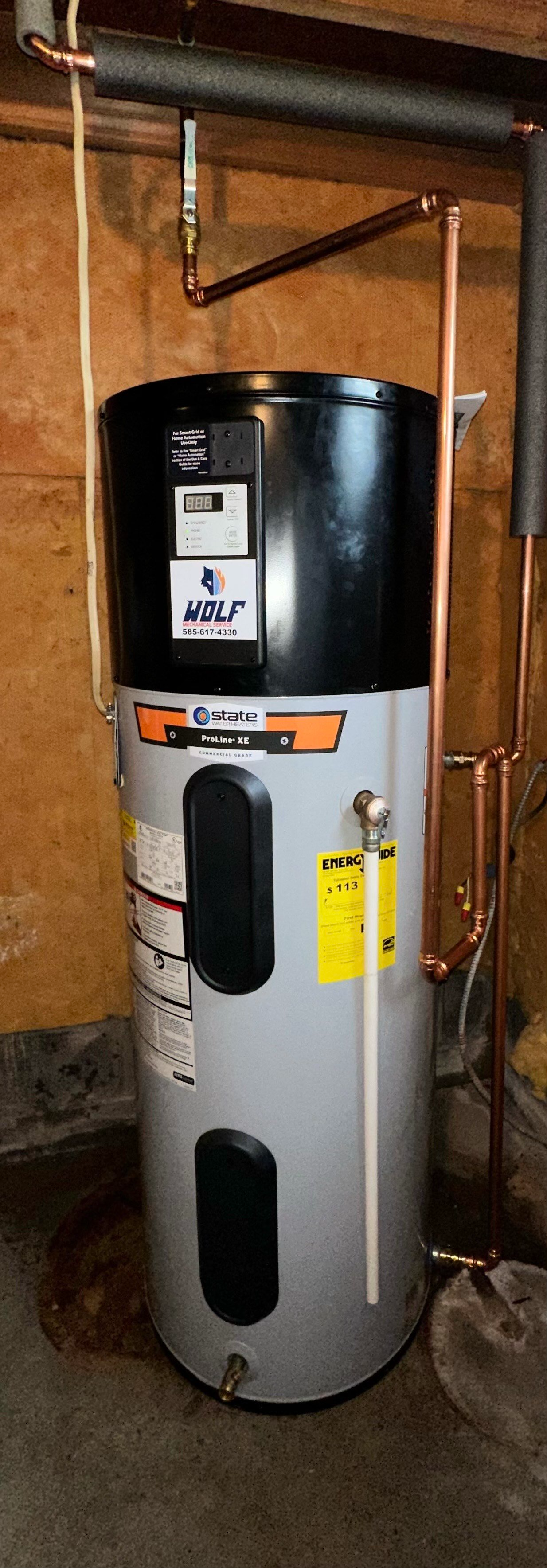 A water heater is sitting in a basement next to copper pipes.