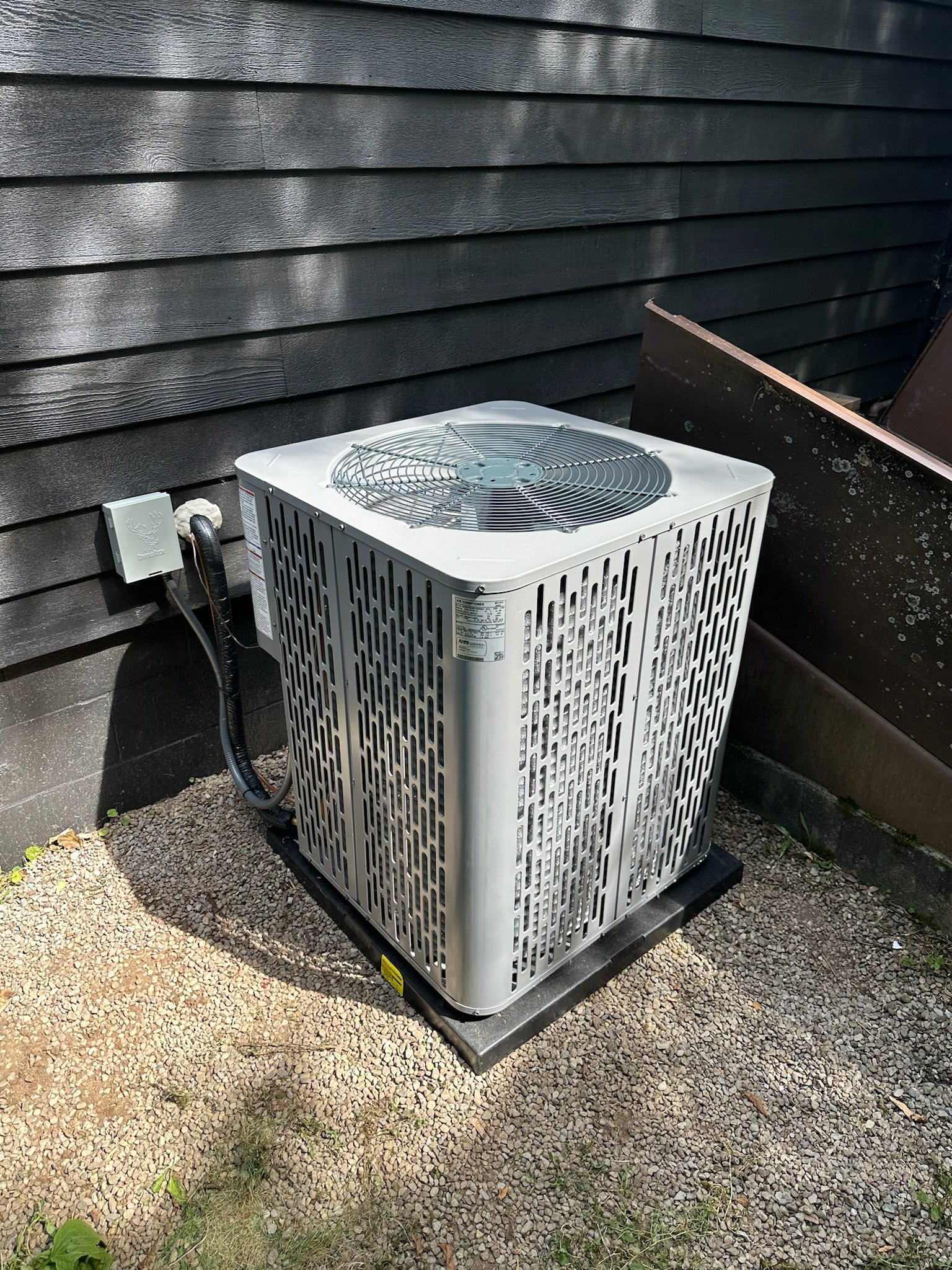 A white air conditioner is sitting on the ground outside of a house.