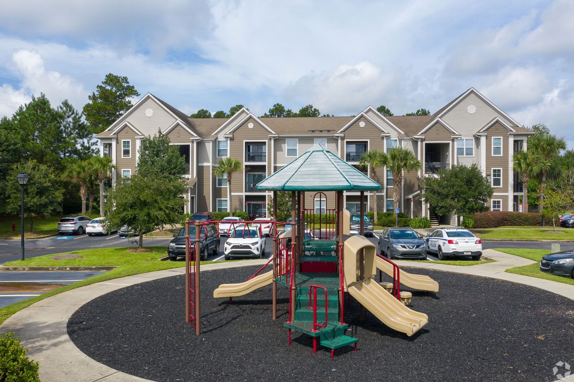 Apartment complex playground with slides and climbing structure in front of parked cars at The Carlyle at Godley Station apartments in Pooler, GA.