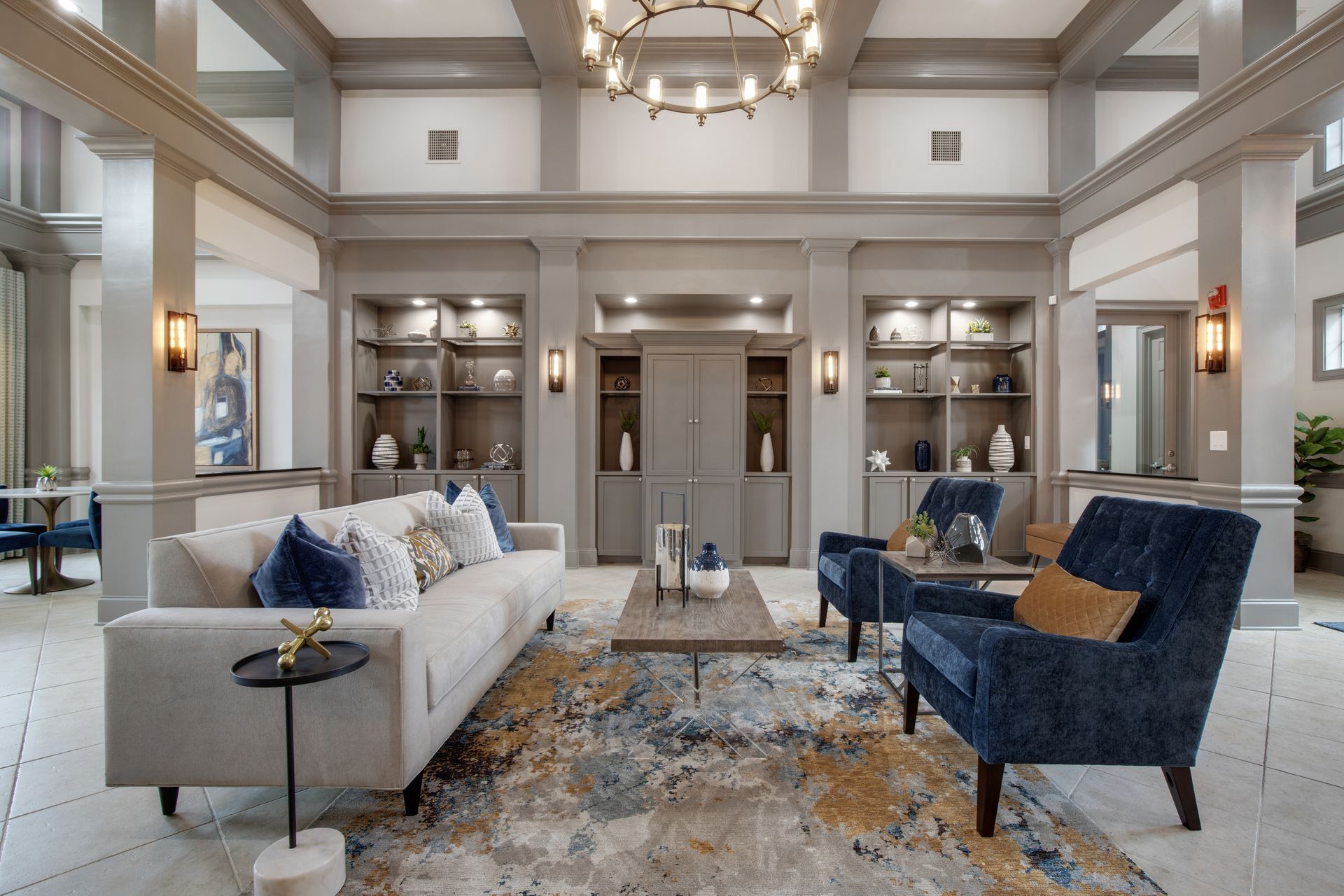 Elegant living room with gray sofas, blue accent chairs, patterned rug, and built-in shelves at The Carlyle at Godley Station apartments in Pooler, GA.
