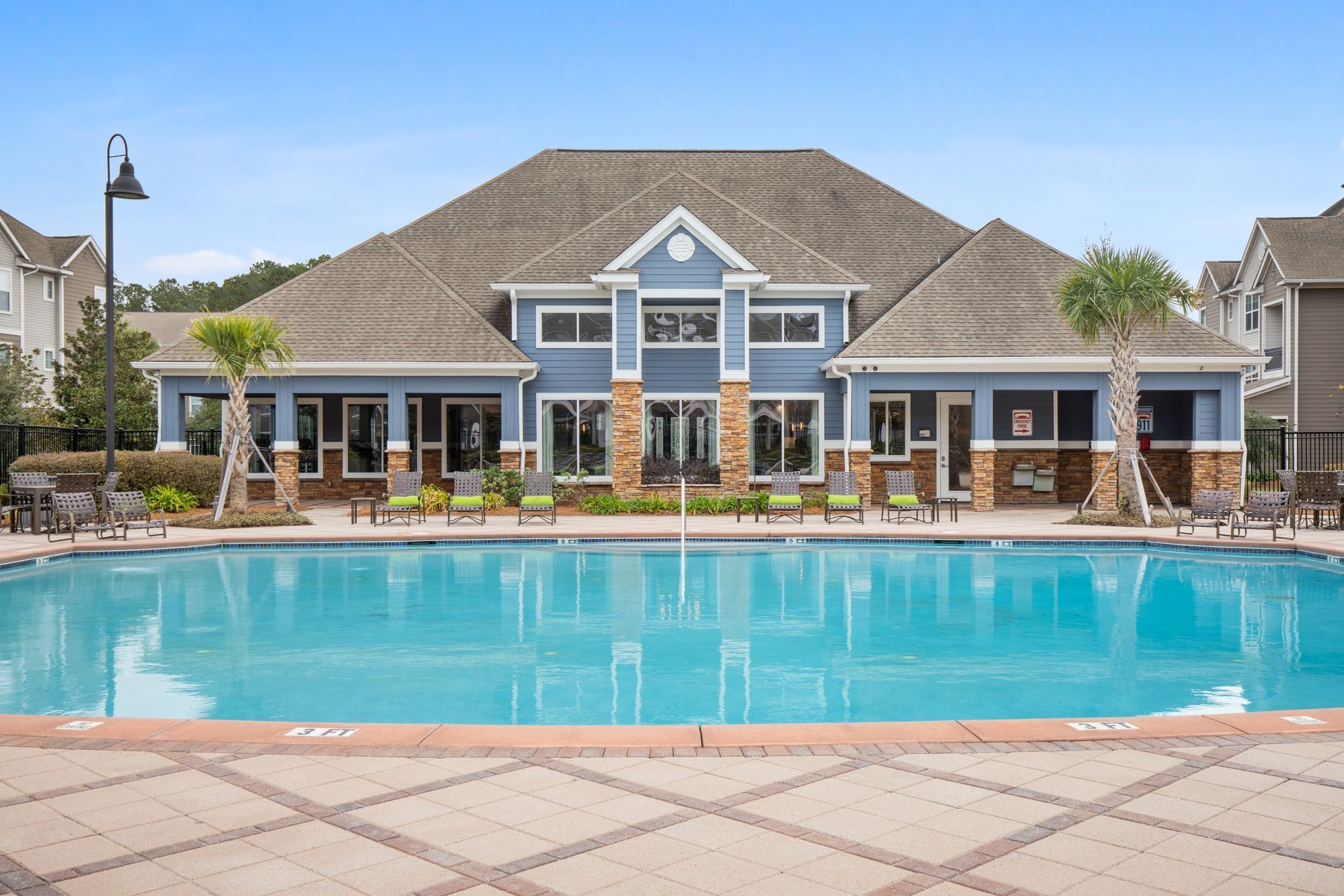 Apartment complex with a large turquoise swimming pool and patio in front at The Carlyle at Godley Station apartments in Pooler, GA.