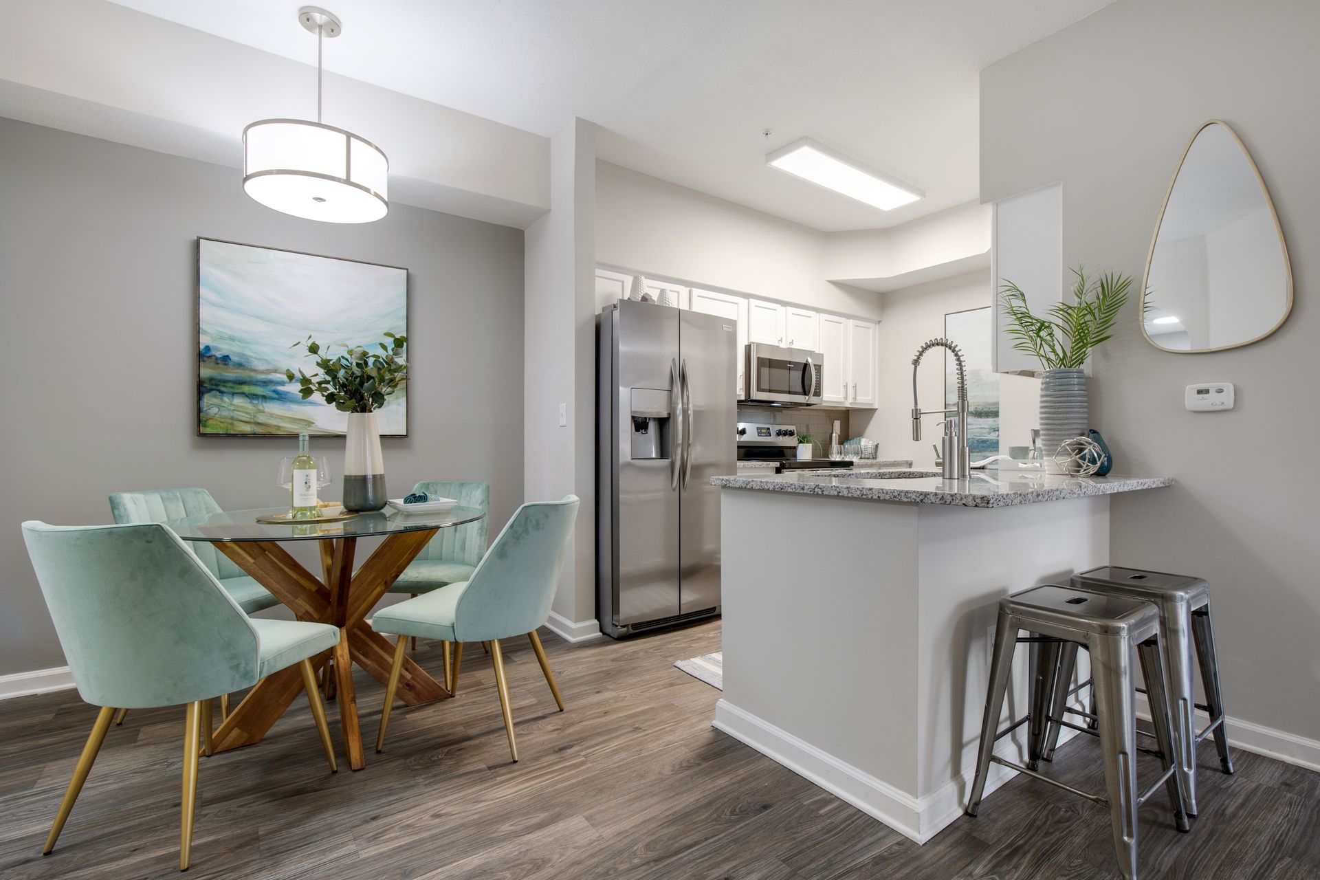 Modern kitchen and dining area with stainless steel appliances, white cabinets, and light blue chairs at a glass table at The Carlyle at Godley Station apartments in Pooler, GA.