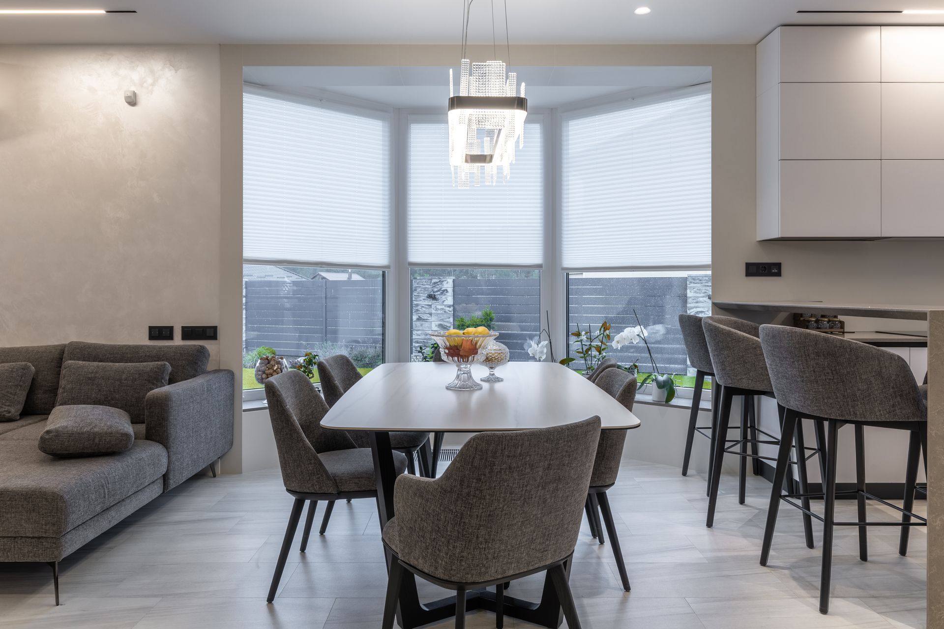 Modern open-plan dining room with gray sofa, table, chairs, and city view through large windows