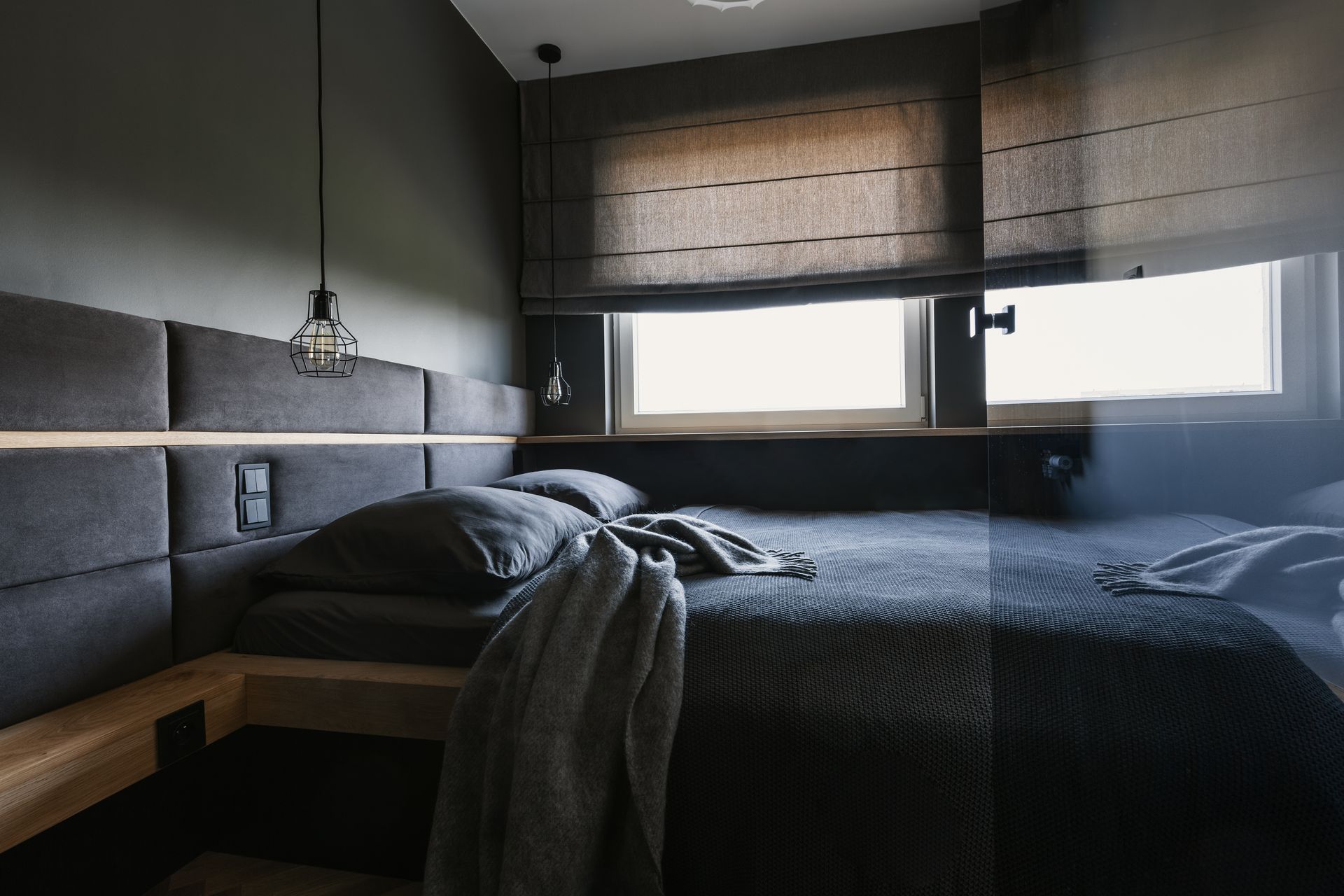 Minimalist bedroom with dark bed, gray bedding, and large windows with woven blinds