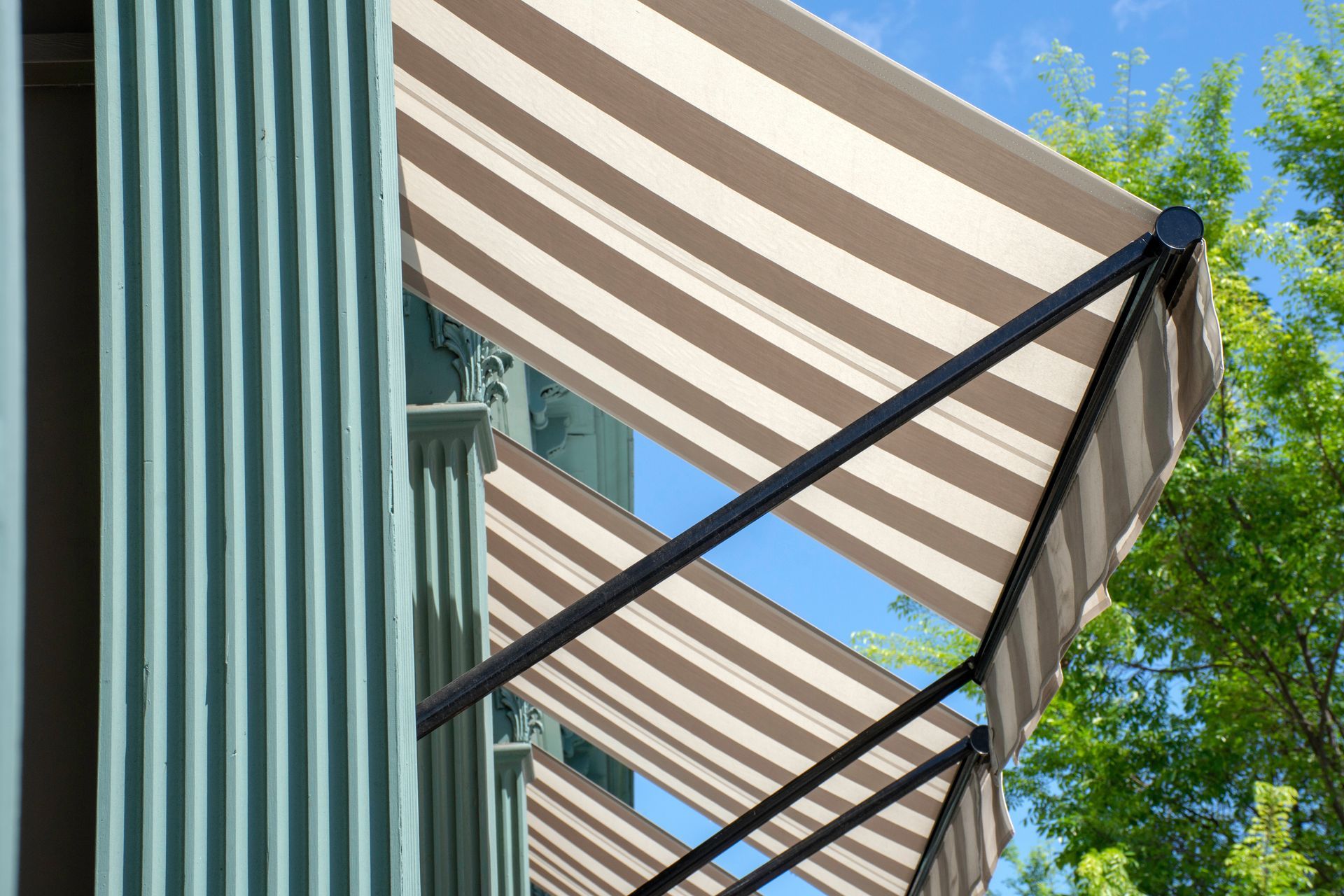 Striped awnings on a building facade beside a blue sky and leafy trees